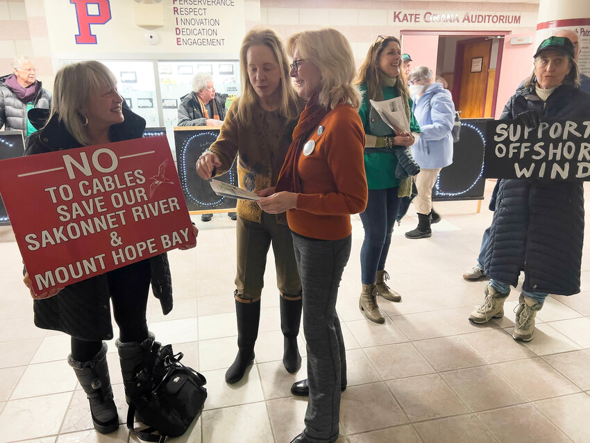 Carol Mello of Portsmouth (left) and Constance Gee of Westport (third from left), who oppose SouthCoast Wind&rsquo;s proposal, hand out work sheets while one of the wind energy supporters, Jill Gabrielsen (right), shows how she feels outside the Portsmouth High School auditorium before Tuesday&rsquo;s Town Council meeting.