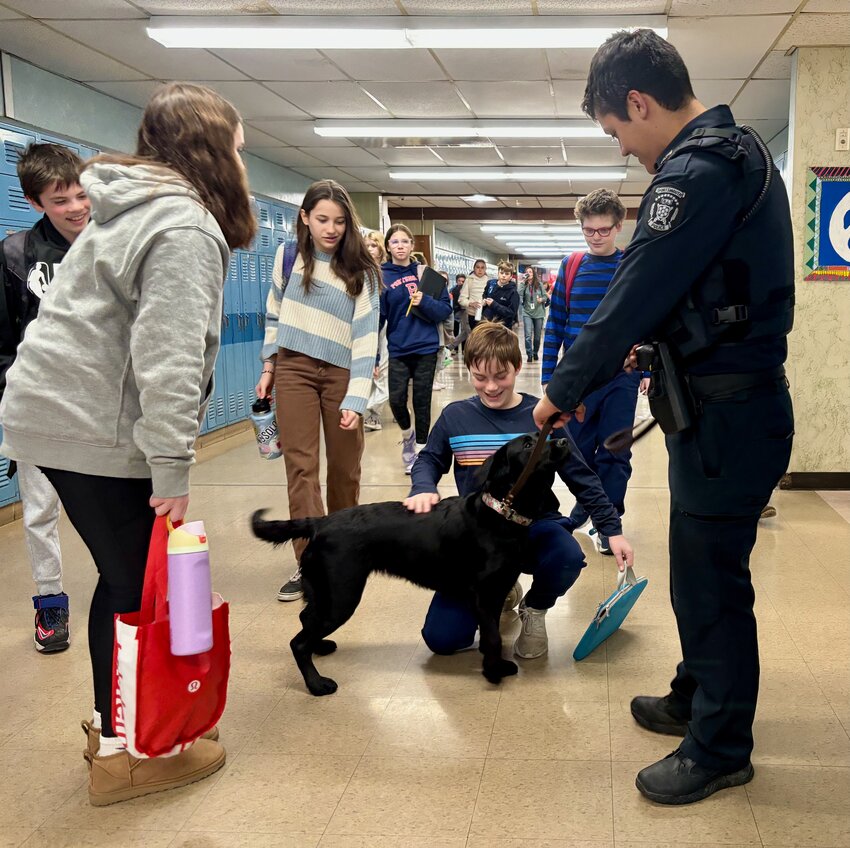 Between classes at Portsmouth Middle School on Monday, Connor Urban pets &ldquo;Officer Holly,&rdquo; the district&rsquo;s new comfort dog, as her partner and School Resource Officer Westley Lemar holds her leash. Also pictured are Caroline Clooney (gray sweatshirt), Maria Walker (blue and white stripes), and Jeffrey Dunn (blue and black stripes).