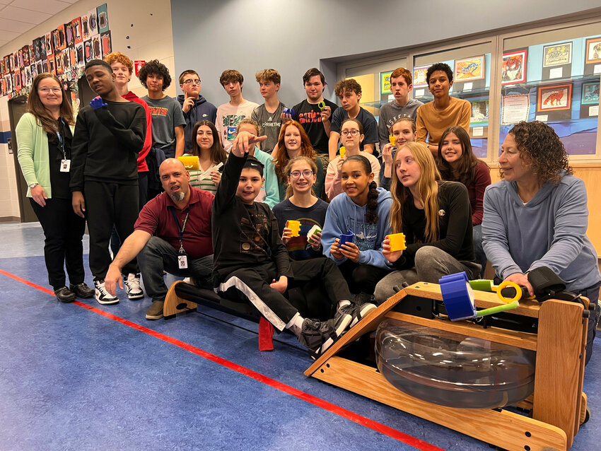 Students in Rebecca Henderson&rsquo;s STEAM Studio class pose for a photo with Ben Orent, while he sits on a rowing machine. Students in the class designed and built special handles that make it possible for Orent to use the rowing machine.