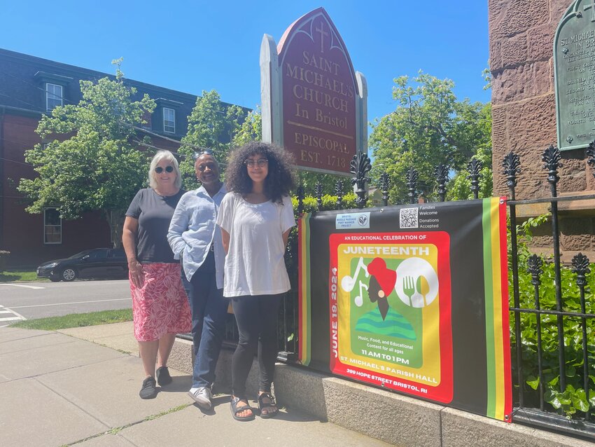 (L-r) Ruthann DeLong, Mattie Kemp, and Yulyana Torres, all members of the Educational, Reconciliation, and Healing Committee of the Bristol Middle Passage Port Marker Project Board, have organized a Juneteenth celebration to be held this Wednesday, June 19. Torres designed this banner, hanging on the fence of St. Michael&rsquo;s Church.