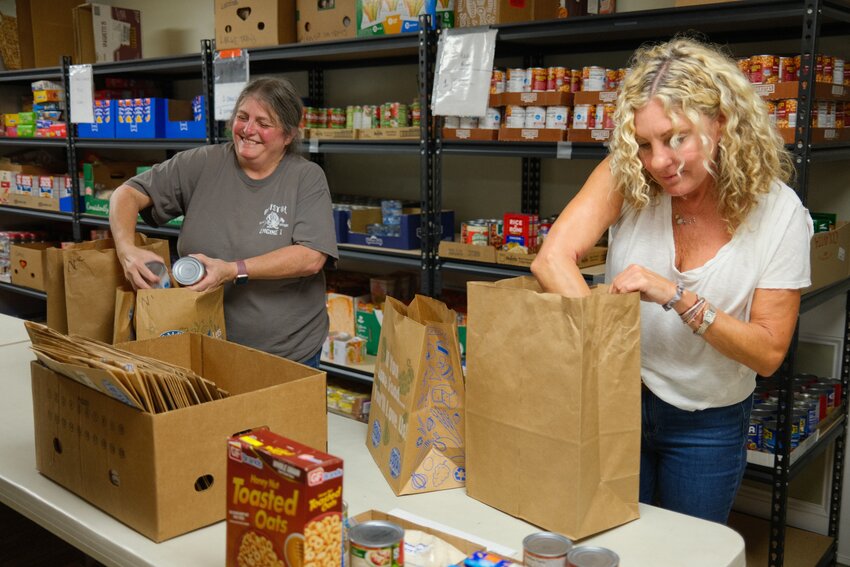 St. John&rsquo;s Lodge Food Bank workers Melody Barnes (left) and new volunteer Christine Tucker load up bags with donated food to give to families in need. Barnes, one of the pantry&rsquo;s directors, decides which food items are selected.