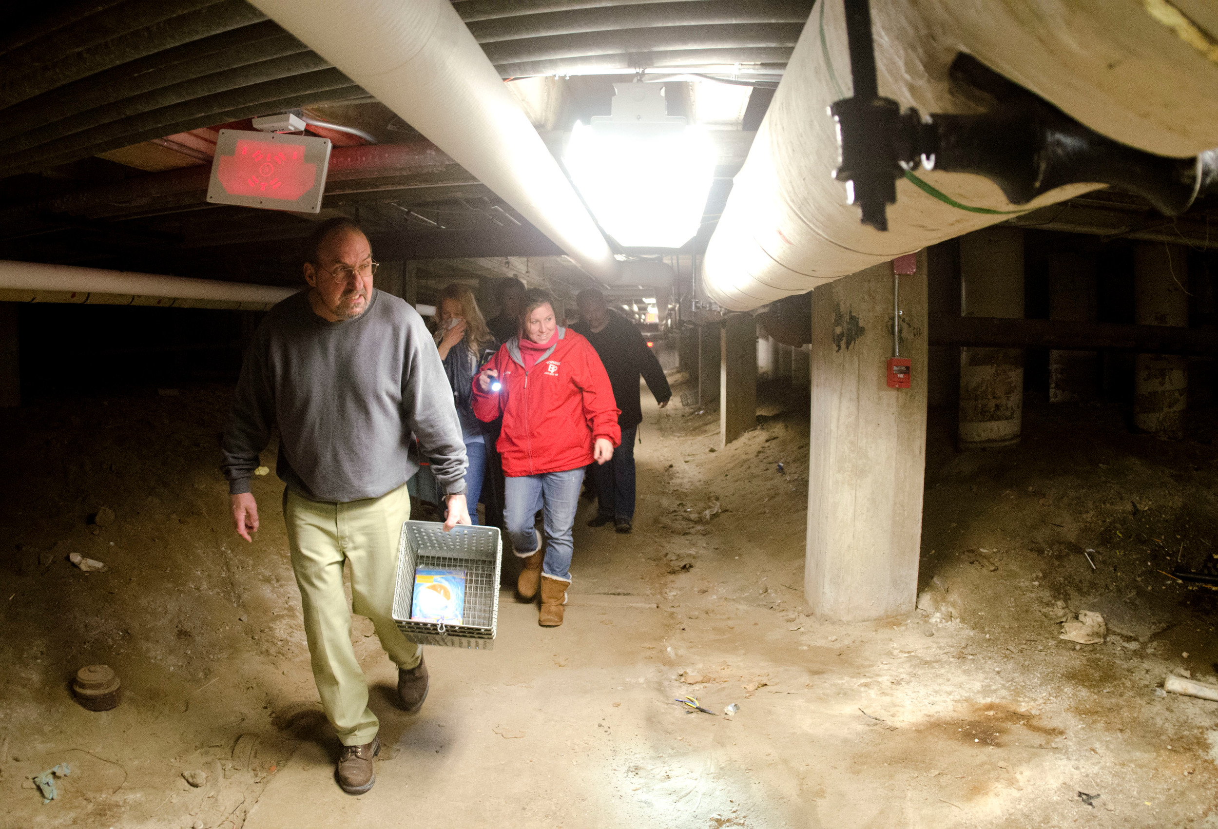 School committee members Anthony Ferreira and Jessica Beauchaine make their way through a dirt path under the 
school leads over to the high school boiler room.