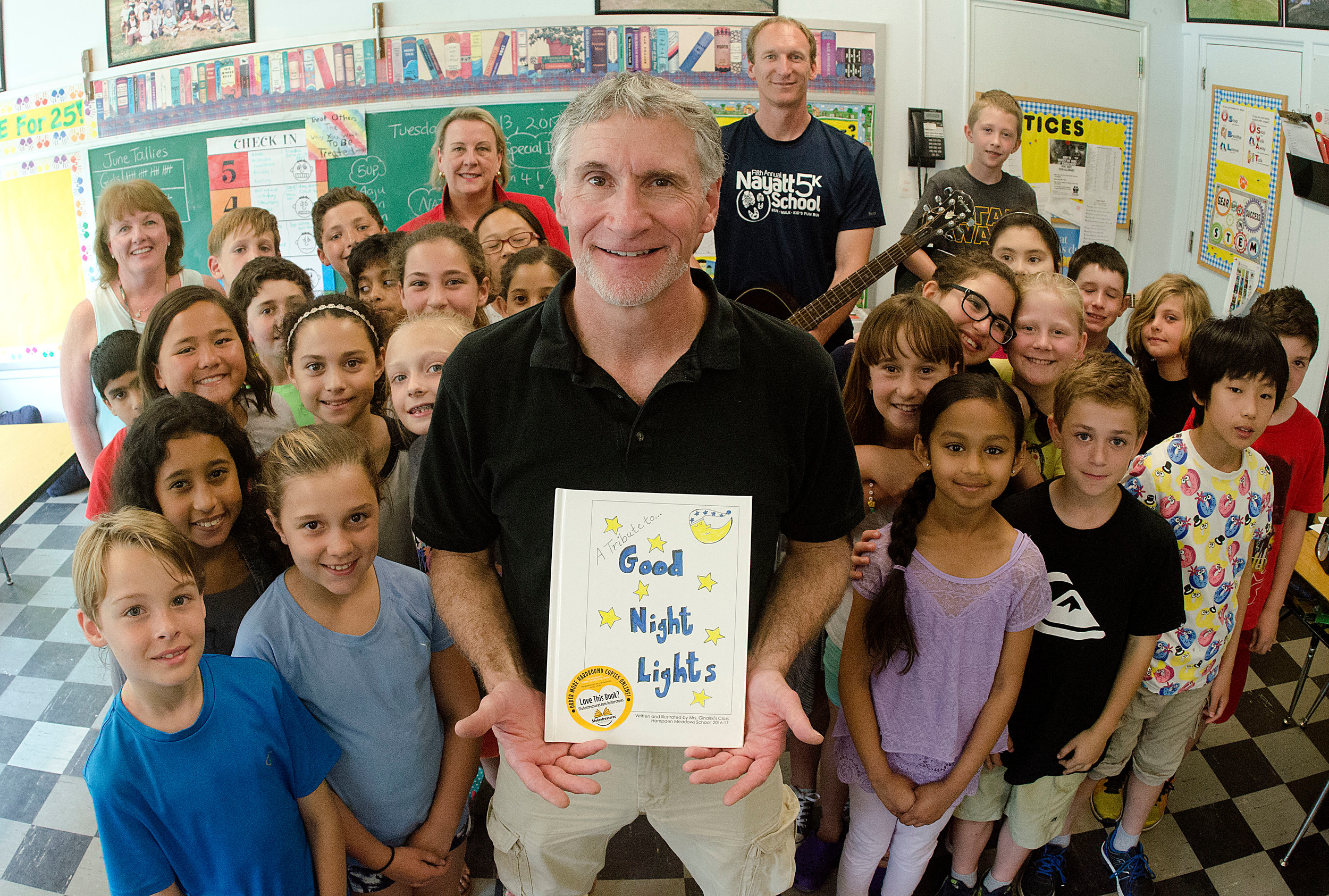 Steve Brosnihan holds a copy of "Good Night Lights" and is surrounded by students and staff from Hampden Meadows School. The students in Mrs. Ginalski's class created the book.