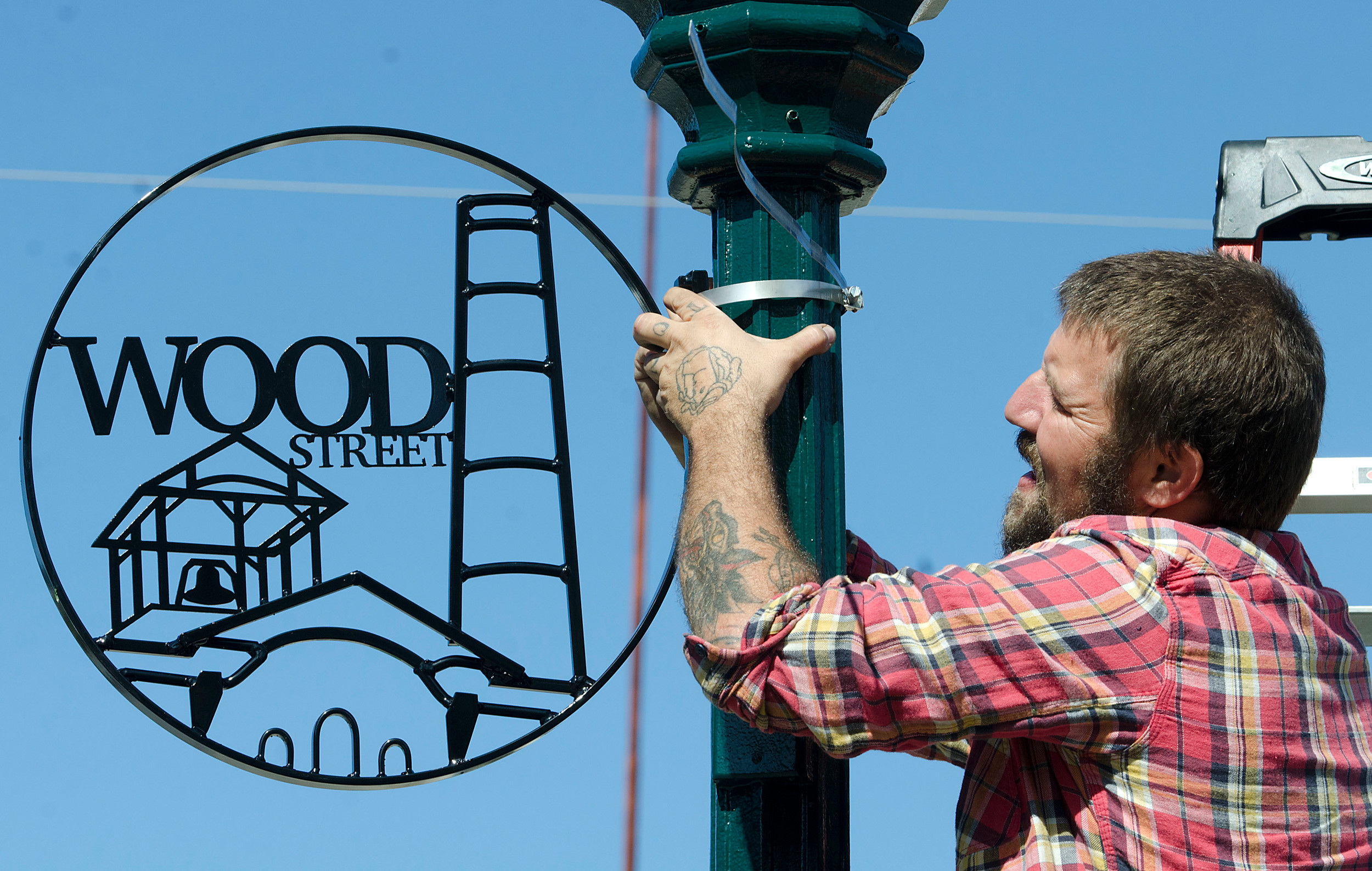 Tim Ferland of the Steel Yard hangs a metal sign that his team designed and made on a Wood Street lamp.