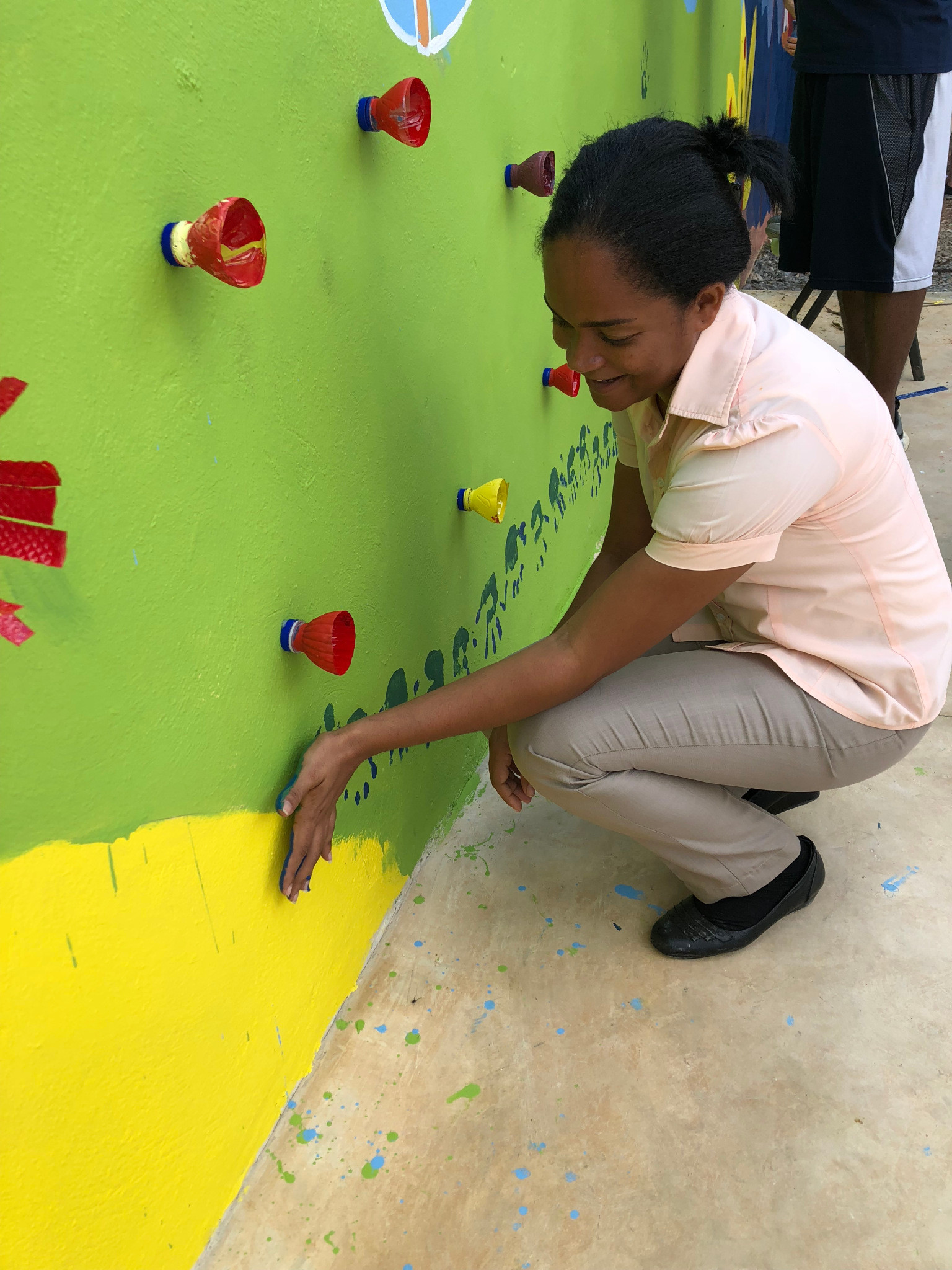 A student uses her handprint to help create a caterpillar on a mural outside a school in the Dominican Republic.