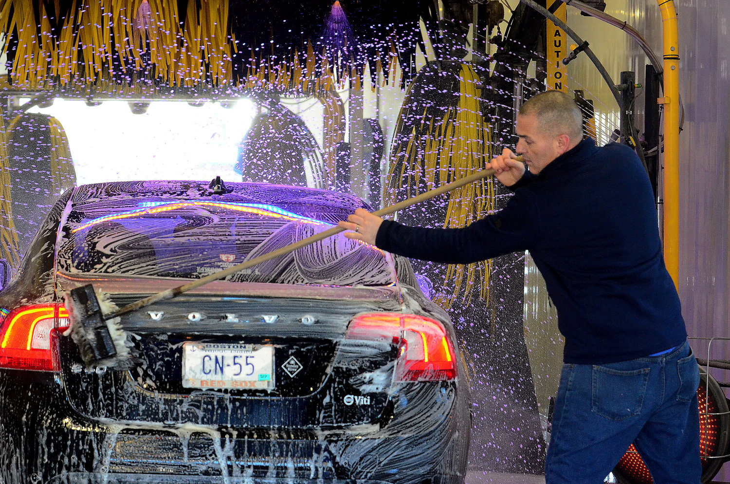 Blue Wave car wash manager Pete Fabiano brushes down a client’s car with a soft cloth as it heads on a track towards the LustraShield surface gloss car wash.
