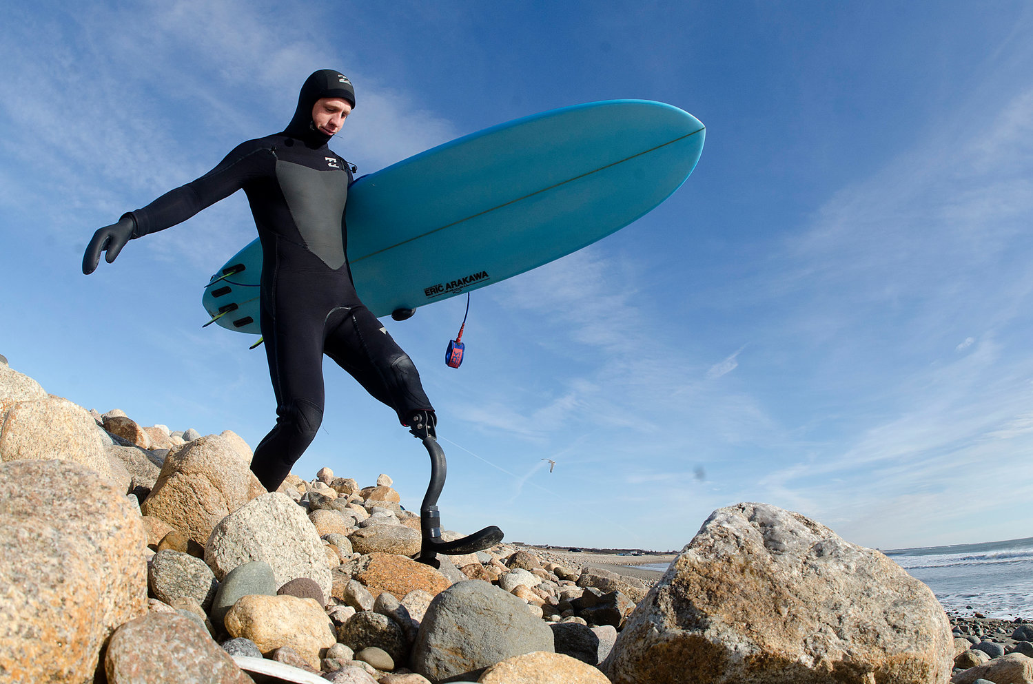 Colin Cook climbs down the rocks at Little Compton’s South Shore Beach nearly two years after the shark attack that claimed part of his left leg. He’s wearing an early-version carbon fiber limb designed and built for him by Sakonnet area friends especially for use while surfing.