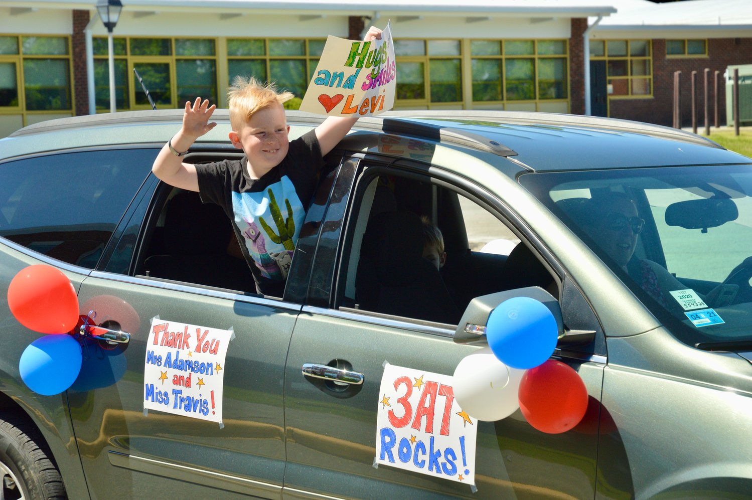 Levi Medeiros, 8, waves to his teacher, Ashley Adamson, during a drive-by parade in the Hathaway School parking lot Tuesday. His mother, Sarahbeth Medeiros, is behind the wheel.