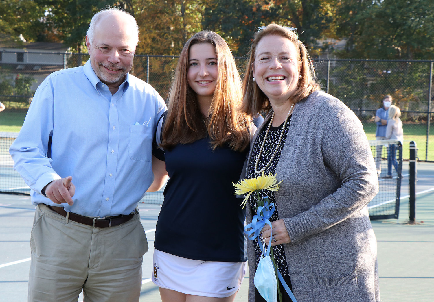 Alison Kostas brings a flower and poses with parents Jude and Susan Kostas during a short senior ceremony at the courts on Friday afternoon.