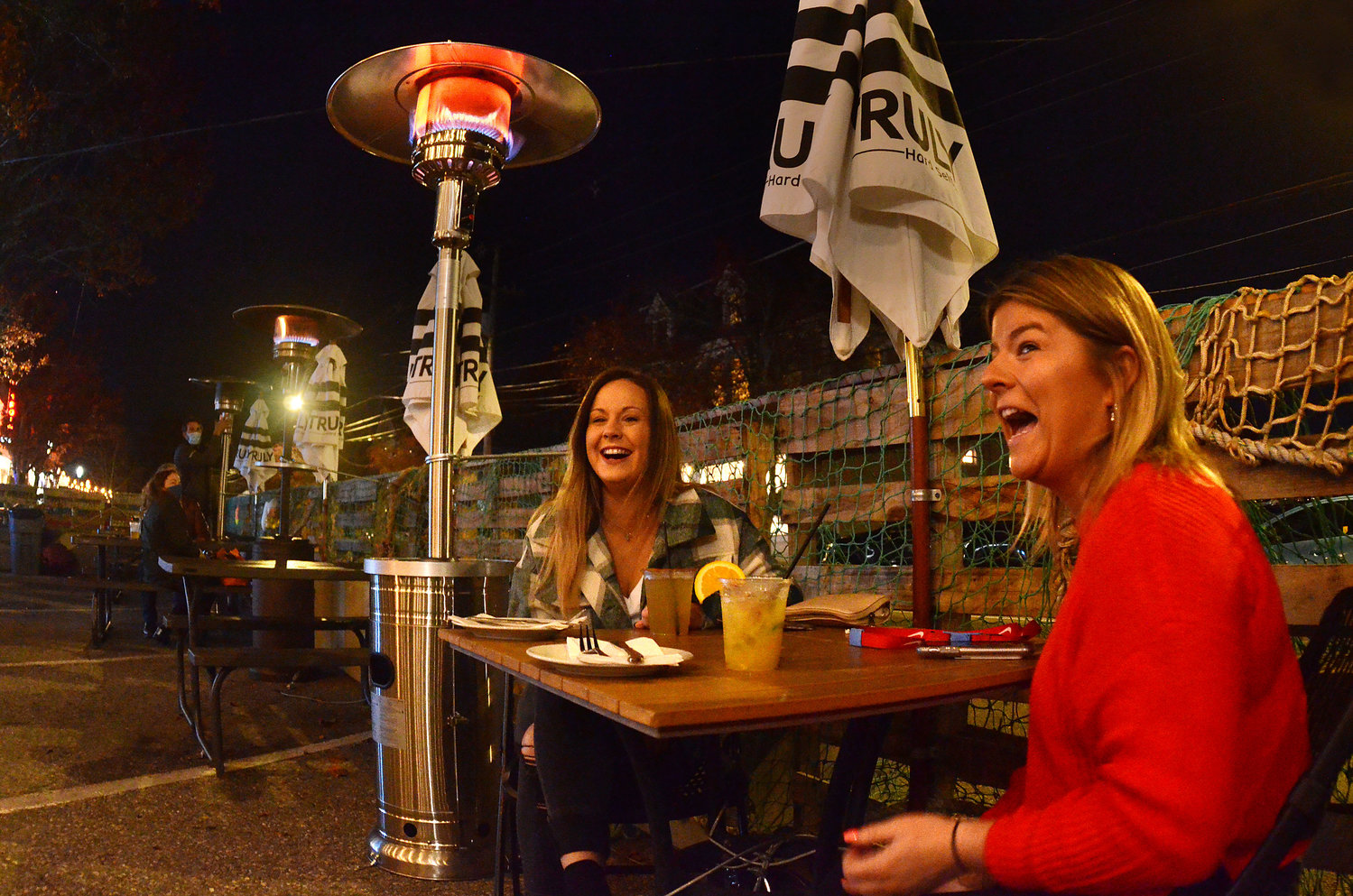 Amber McCollum (left) and Kaitlan Mitchell share a laugh, and some warmth, under a new patio heater outdoors at Judge Roy Bean Saloon on Tuesday. 