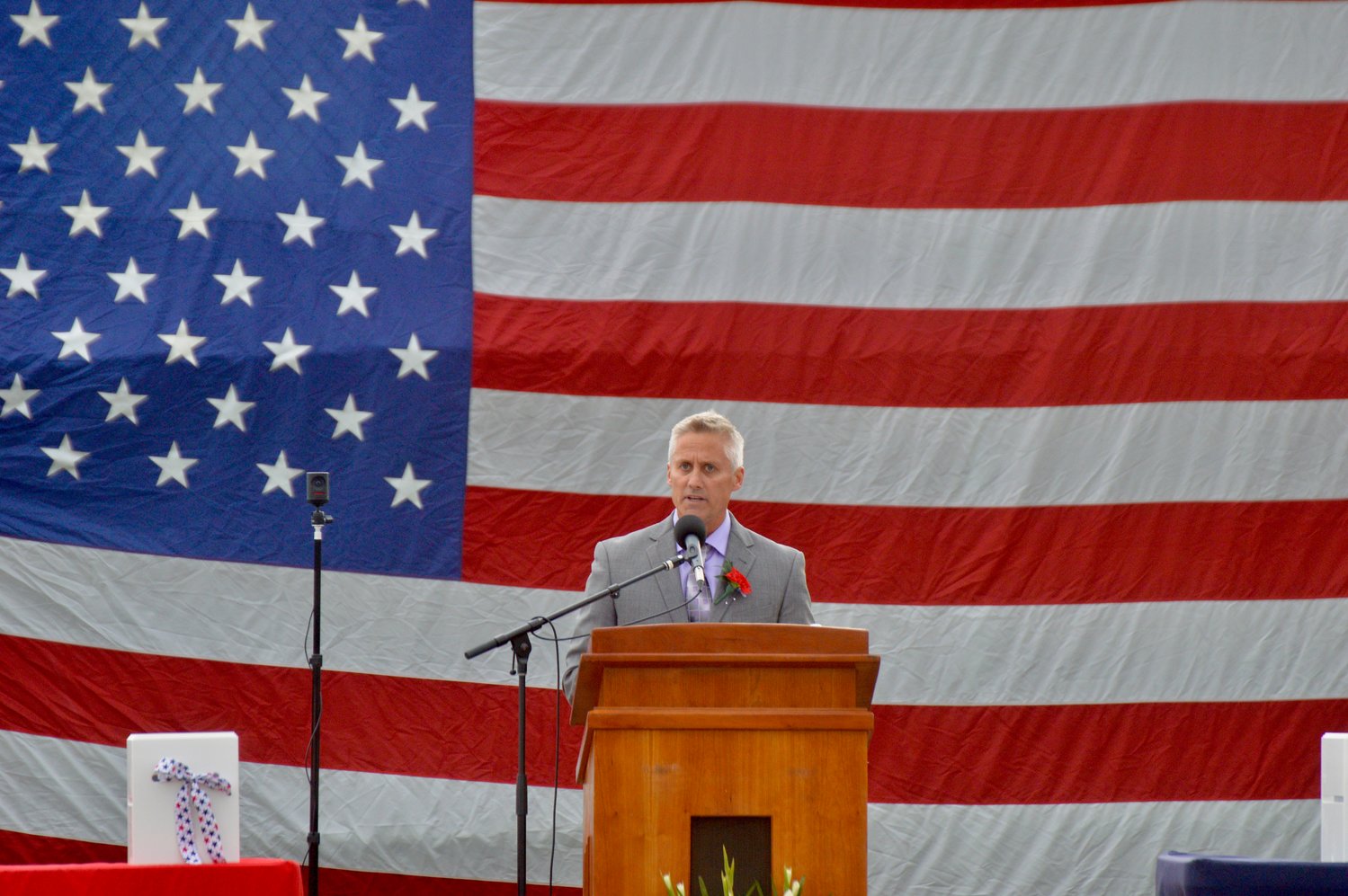 Guest speaker Rusty Forgue addresses graduates as a giant American flag provides the backdrop.