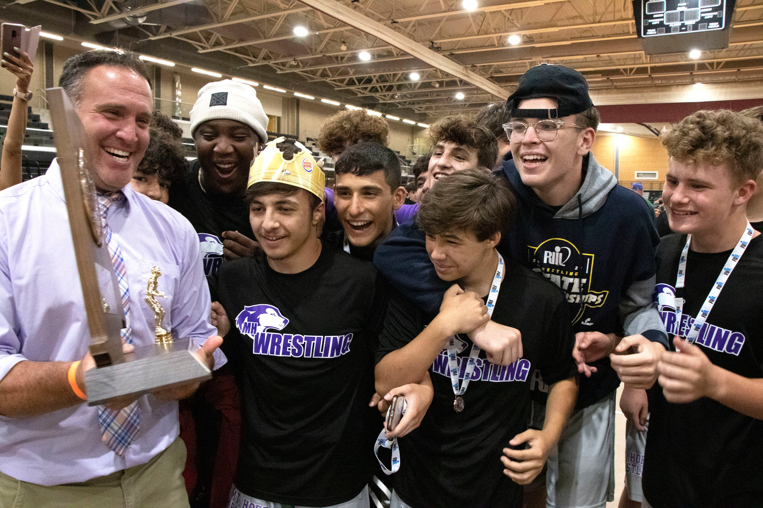 Coach Eric Francis shows the team the state championship trophy after their team victory during the wrestling state tournament on Saturday.