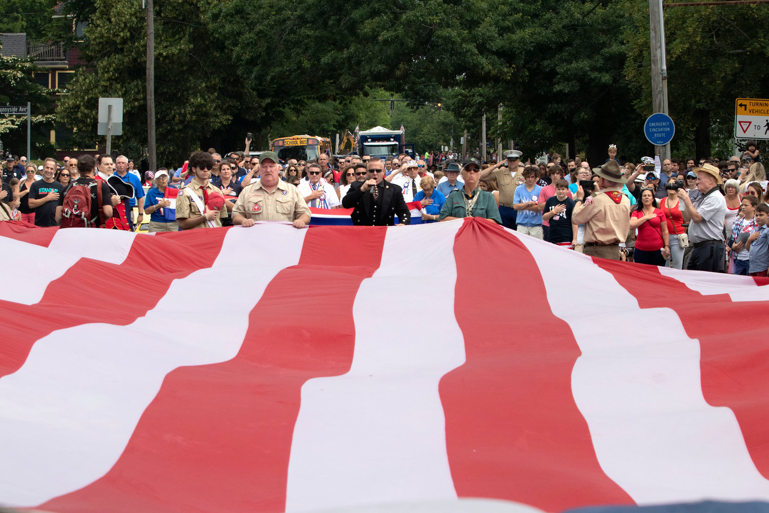 The Singing Trooper, Daniel Clark, leads the crowd in the National Anthem at the opening ceremony for the 2021 Bristol Fourth of July Parade, just before the procession stepped off from the intersection of Hope and Chestnut streets. The enormous flag was carried down the two-and-a-half-mile route by Scout troops.