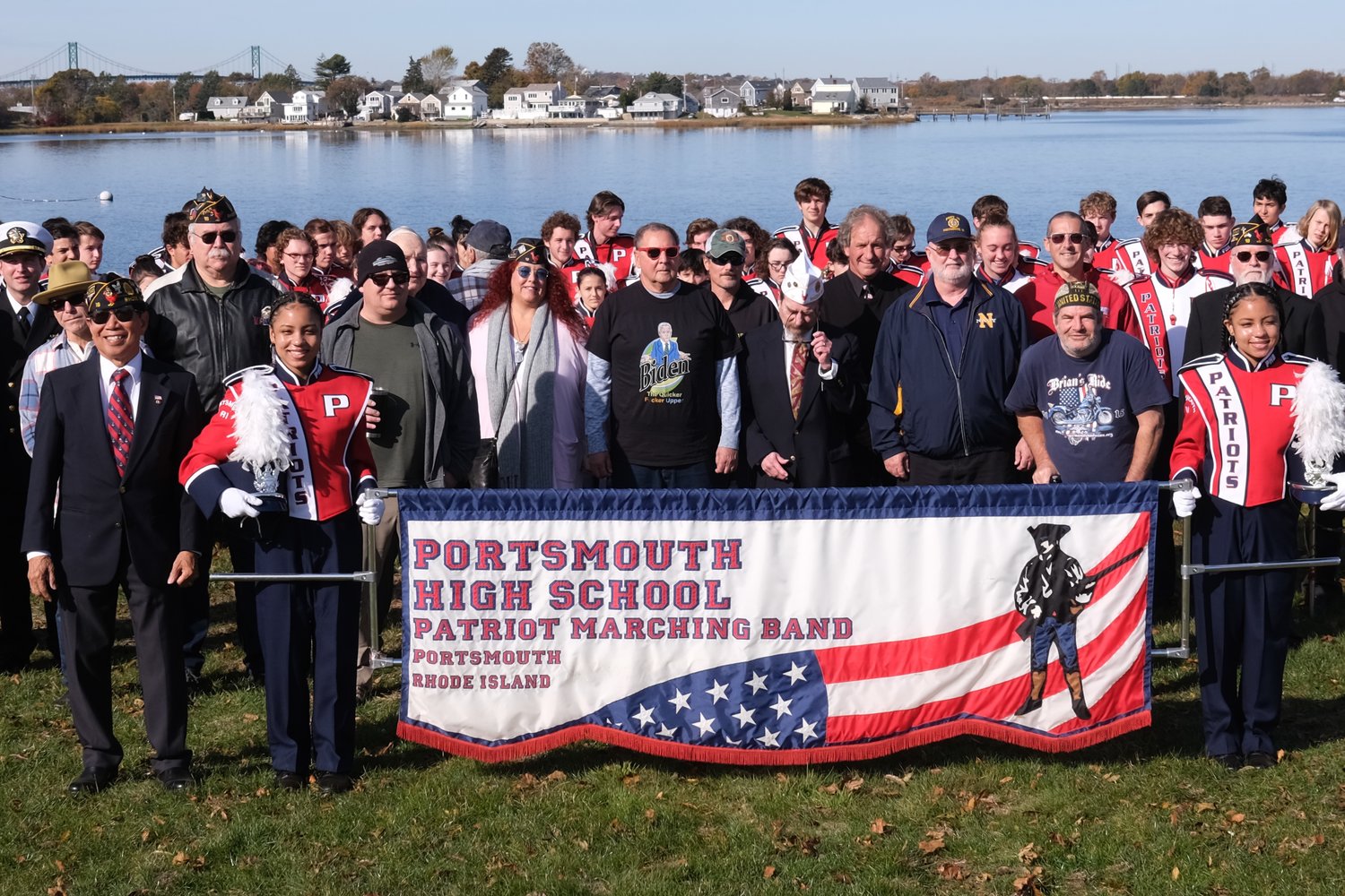Members of the PHS Marching Band pose for a photo with local veterans on the back lawn of Thriving Tree Coffee House, overlooking Blue Bill Cove. Identical twins and PHS sophomores Makayla (left) and Keira Boxell are holding the banner.