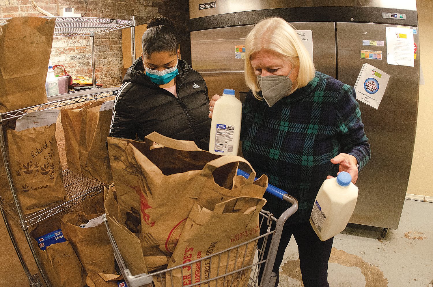 East Bay Food Pantry volunteer Lynn Carlson places two cartons of milk into a bag for client Mishelly Santiago last Wednesday.