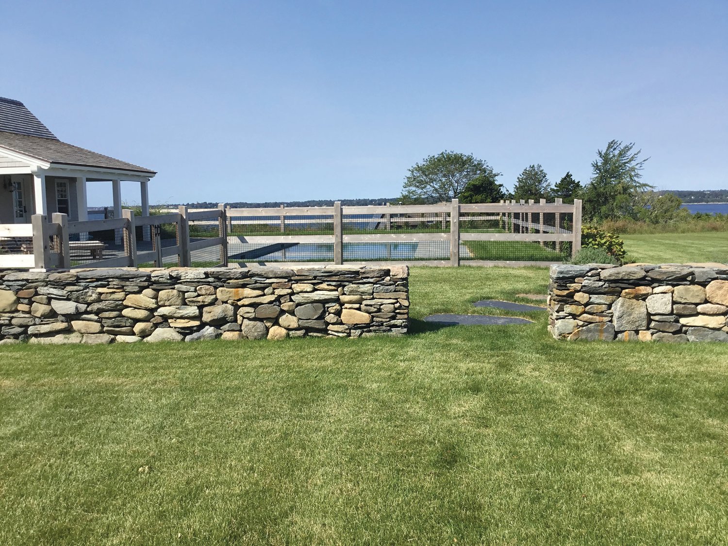 The new stone wall encircles an area of the property featuring a newly constructed barn, pool house and pool. Seen here, the wall under construction, and the finished product, with views out over the Sakonnet River.