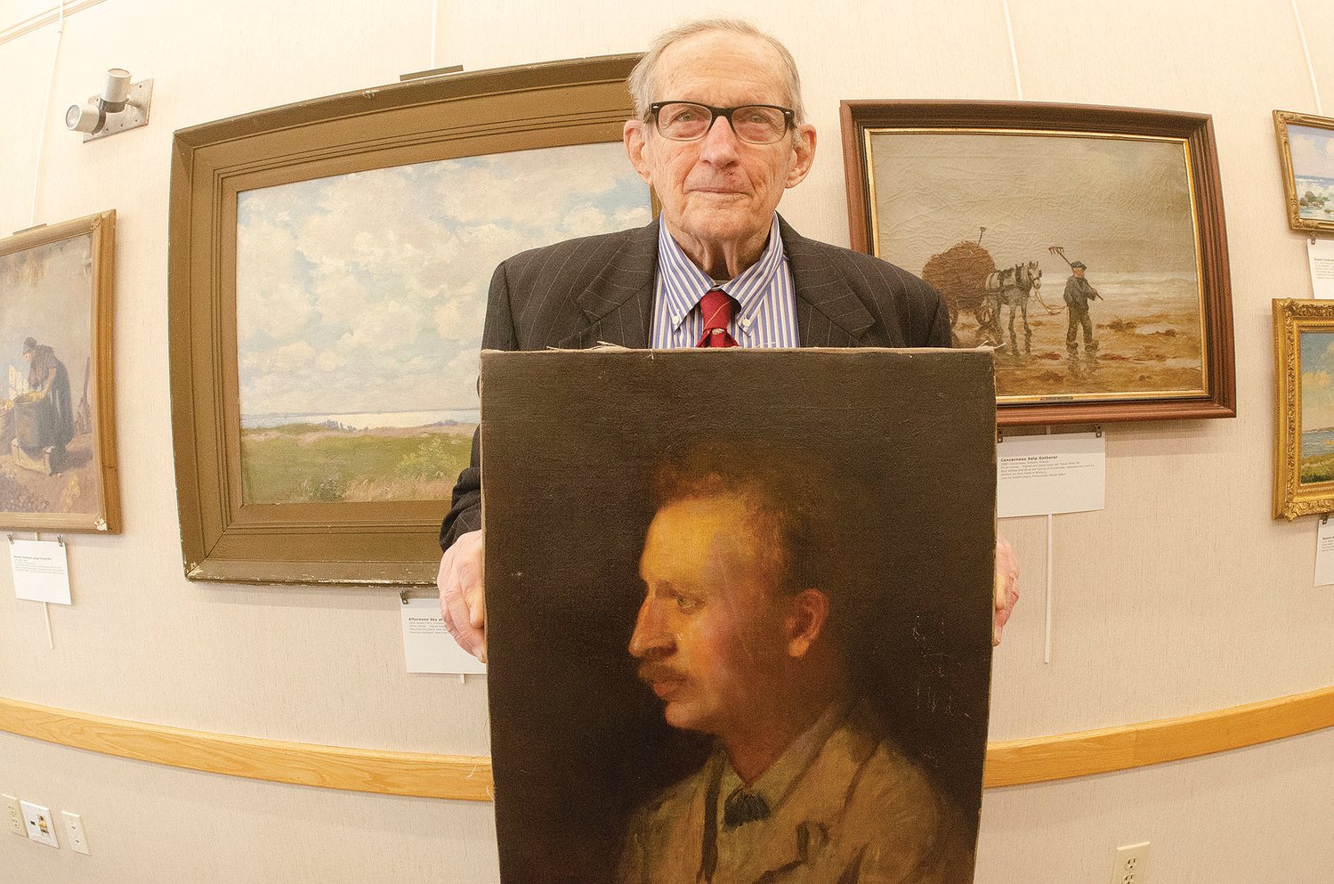 August Miller holding a portrait of his grandfather, Oscar Miller, painted by Emmanuel Fox. The other 14 paintings in the exhibit, on display through January at the Portsmouth Public Library, show Oscar’s impressive range of style and technique, developed in his years of travel throughout the U.S. and Europe.