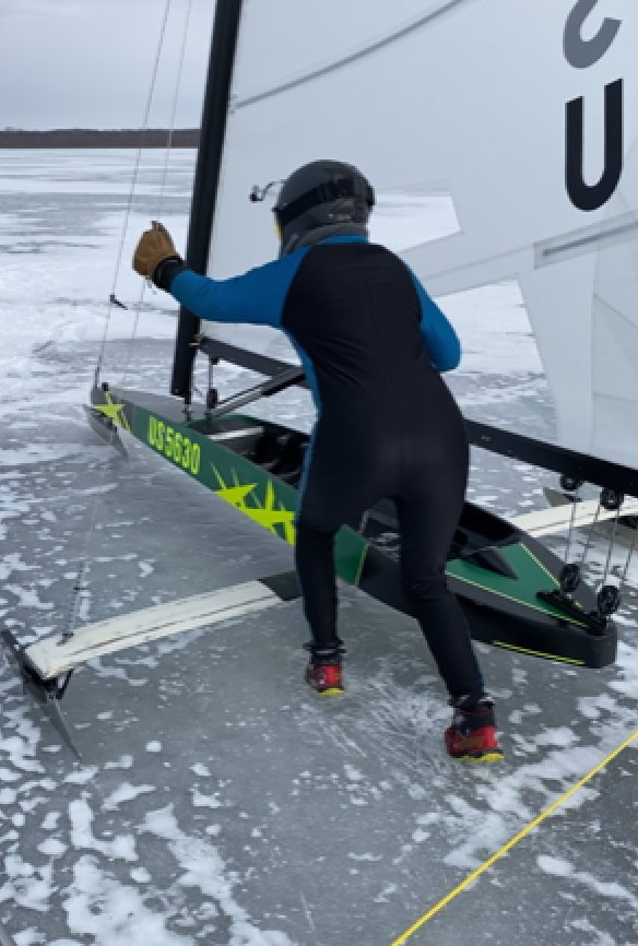 Karen Binder starts a race at the 2022 DN US Nationals. Similar to the start you might see at an Olympic bobsledding event, competitors (wearing spikes on their feet) push start their boats before catching the wind.