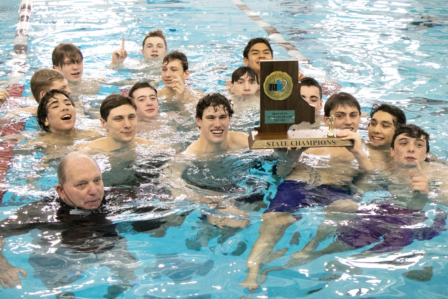 The Barrington High School boys swim team won the state championship on Saturday morning, March 5, at Brown University. Here, Coach Sandy Gorham holds the state championship trophy surrounded by members of the boys team.