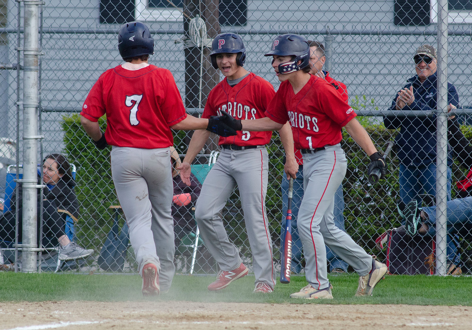 Shane Harvey (left) and teammates Caleb Banks and Dave Spigel celebrate as Harvey crosses the plate in the fourth inning to give the Patriots a 1-0 lead last week.
