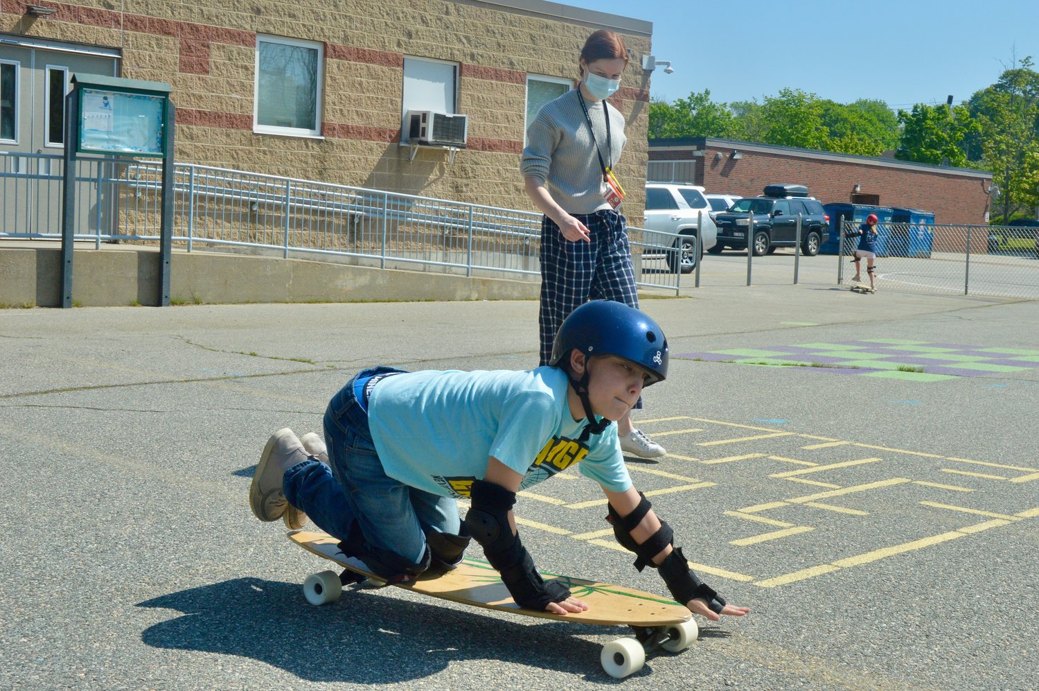 Aiden, a fourth-grader at Melville School, preferred to ride low to the ground on his longboard. Looking on is teacher’s aid Kaitlin Powell.