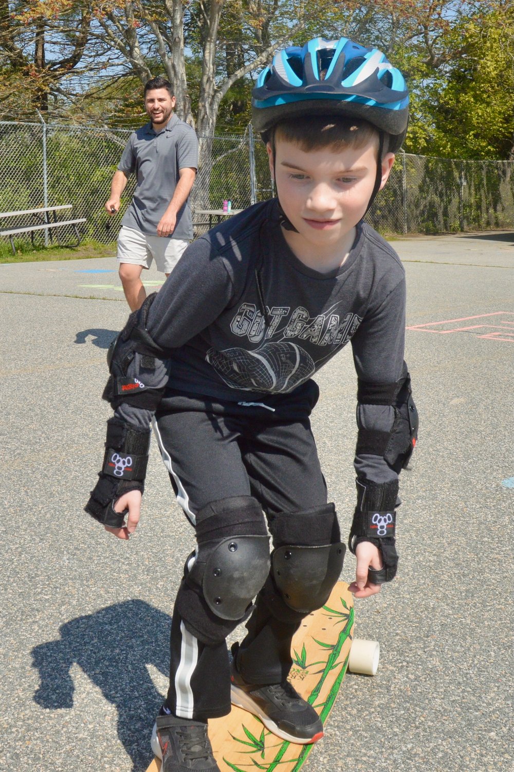 Melville School P.E. instructor Ryan Soares (background) watches fourth-grader Lucas try his hand at the longboard.