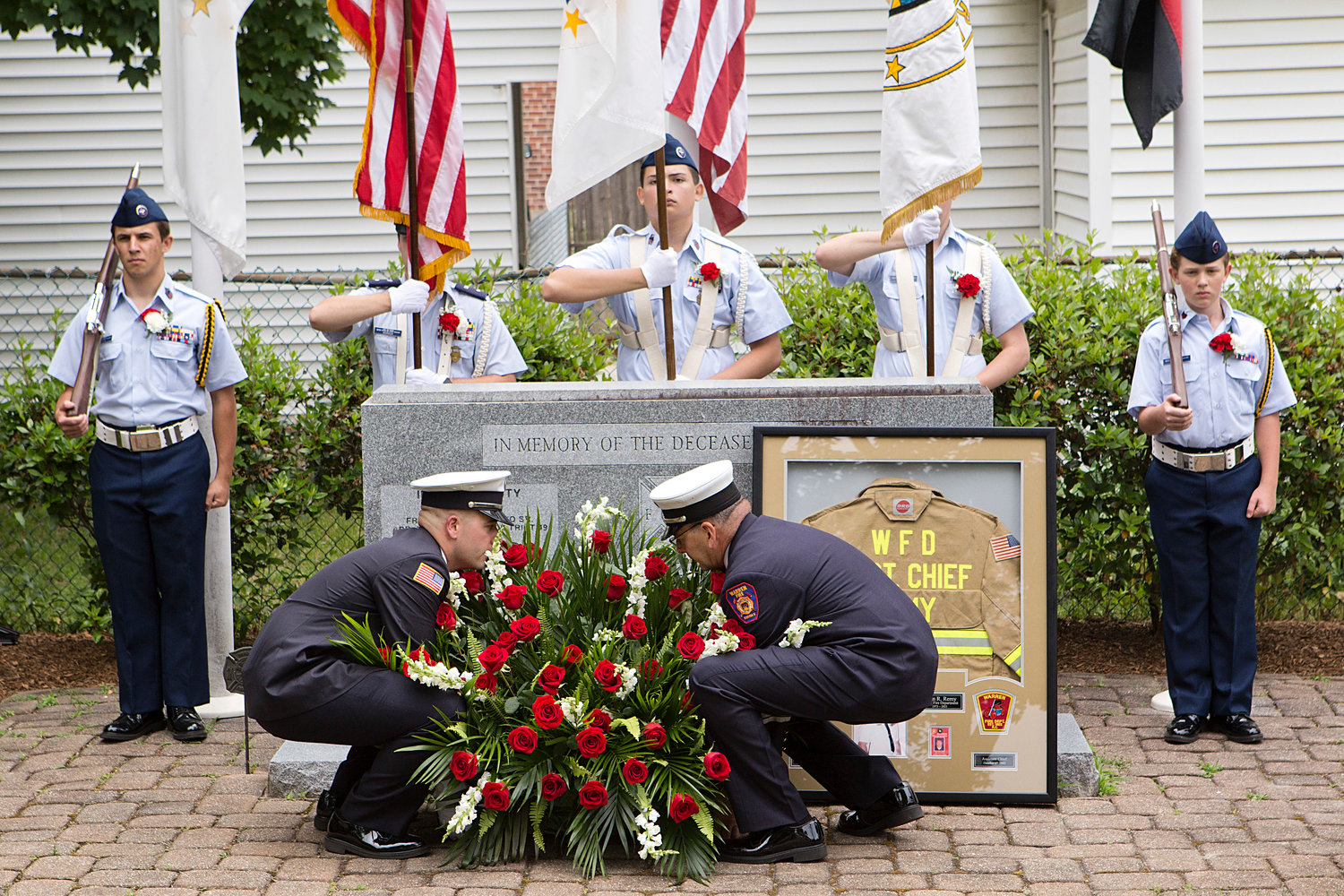 A pair of firefighters place red and white flowers on a memorial site in remembrance of deceased members of the Warren Fire Department, which included a dedication to former Assistant Fire Chief, Brian Remy, who passed away last year.