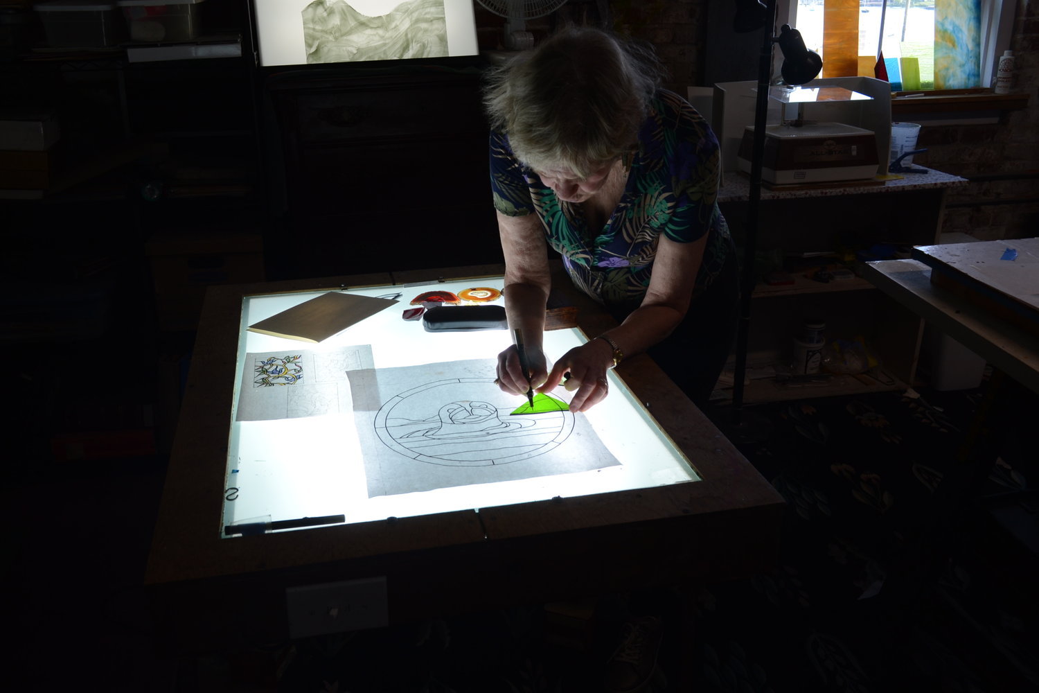 Diana Cole, an artist of many talents, draws a line using a light table onto stained glass prior to scoring and breaking the piece, as part of Art Night’s Meet the Artist series where Cole gave a detailed demonstration on making stained glass art.
