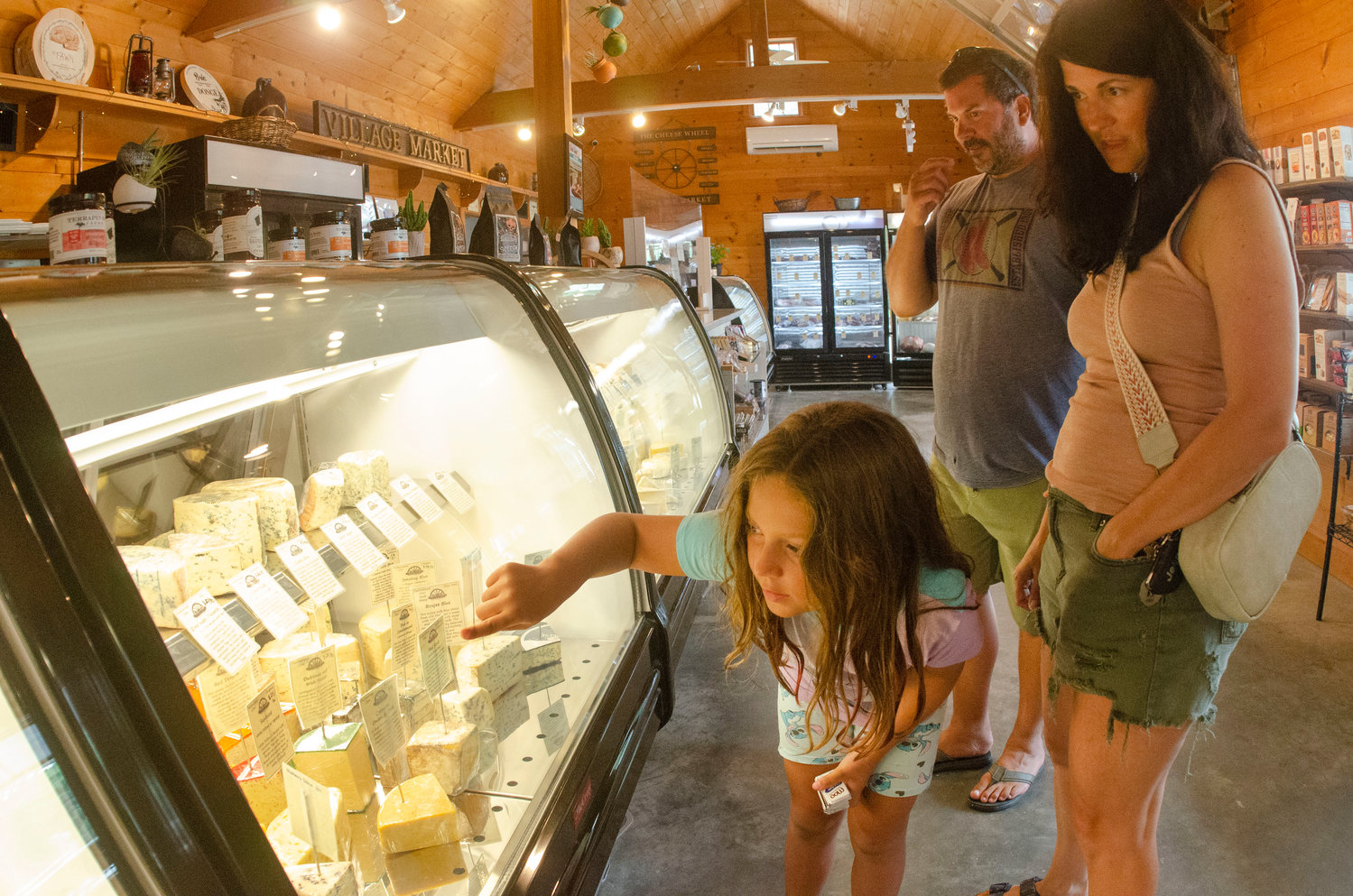 Alta Smith scans a display case at The Cheese Wheel at Tiverton Four Corners with her parents, Christopher Smith and Jennifer Proulx.