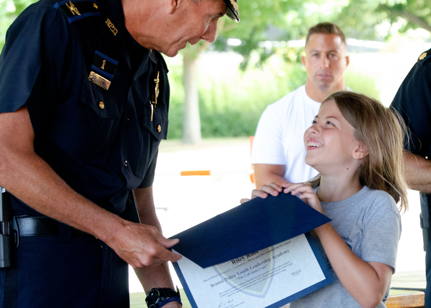Bristol Police Chief Kevin Lynch (left) and Major Brian Burke pose with Riley Ross after she received a certificate for passing the leadership academy at the town beach on Friday.