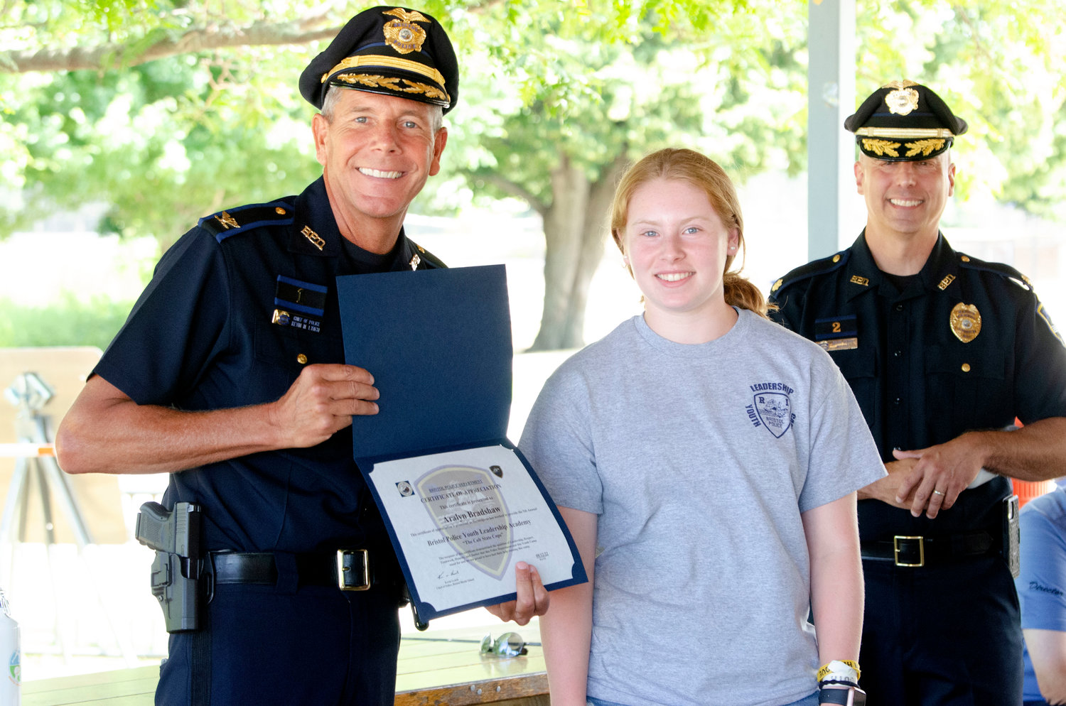 Bristol Police Chief Kevin Lynch (left) and Major Brian Burke pose with Aralyn Bradshaw after she received a certificate of appreciation during the Bristol Police Youth Leadership Academy at the town beach on Friday.
