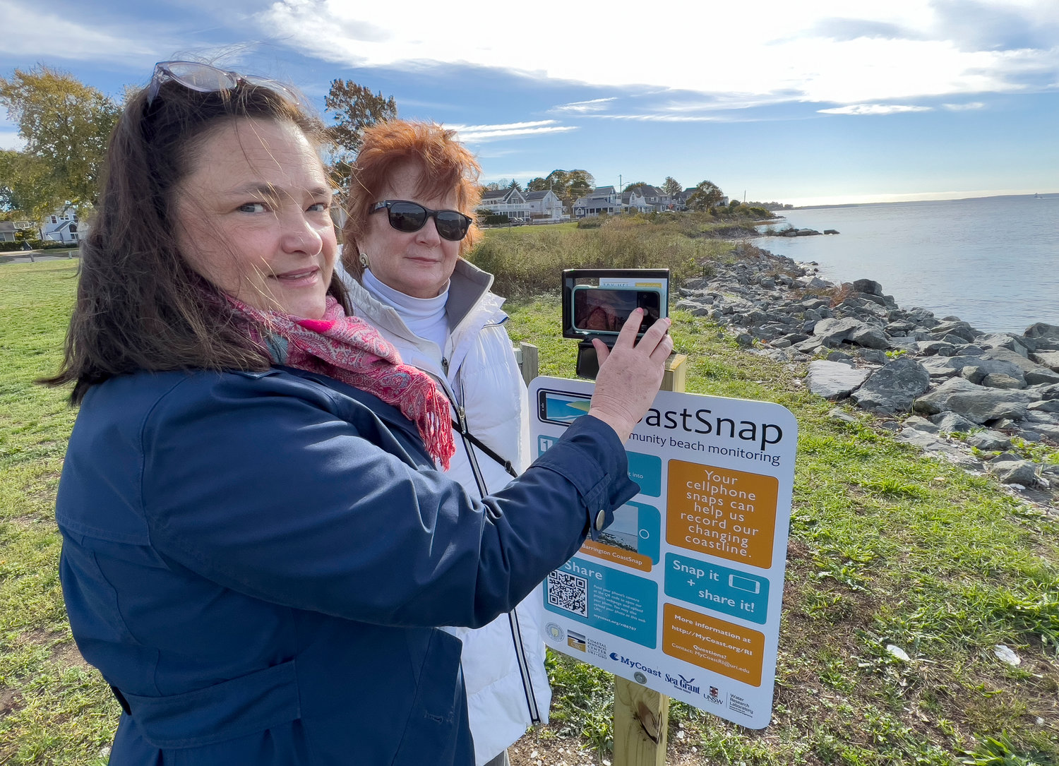 Barrington Town Planner Teresa Crean (left) and Barrington Resilience and Energy Committee member Lynne Carter display the new CoastSnap Station at Latham Park in Barrington.