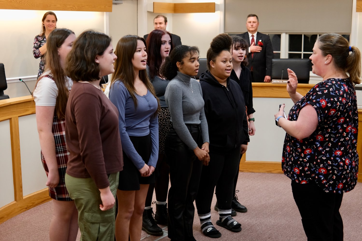 Members of the Portsmouth High School Vocal Ensemble, led by Shawna Gleason, sing The National Anthem at the start of the program. Behind them are Town Council members Daniela Abbott, Andrew Kelly (outgoing) and Keith Hamilton.