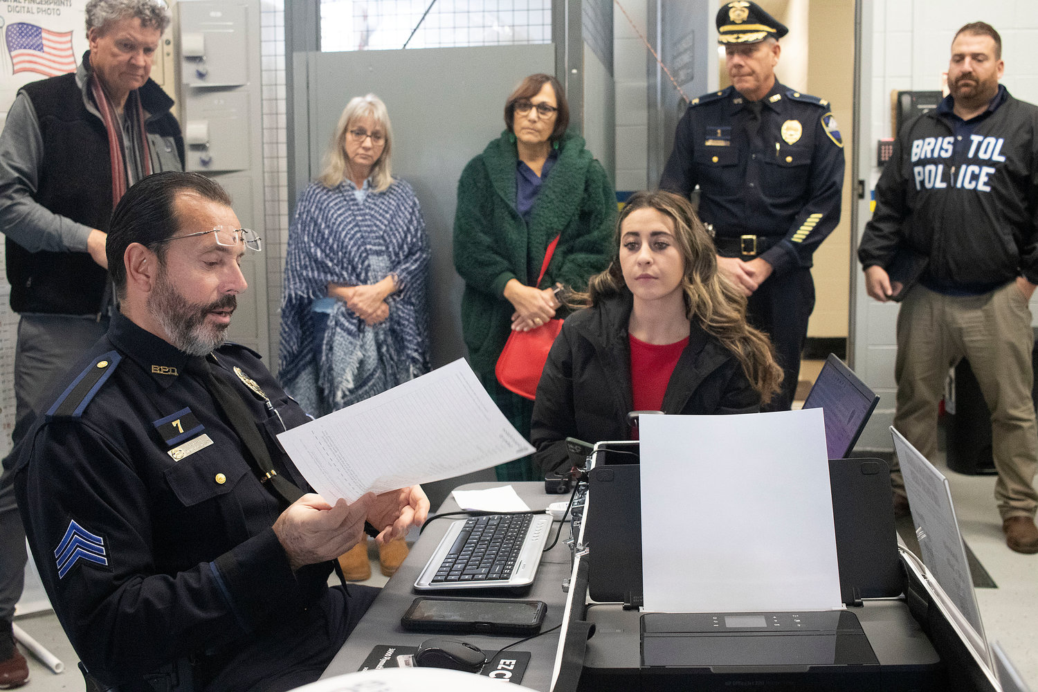 Sgt. Ricardo Mourato demonstrates the process of registering with the Child ID system using Channel 12 reporter Dana Casullo as an example, while (l-r) Sen. Wally Felag, resident Candice Dacosta, Senior Center Director Maria Ursini, Chief Keving Lynch, and Patrolman Brandon Correia look on.