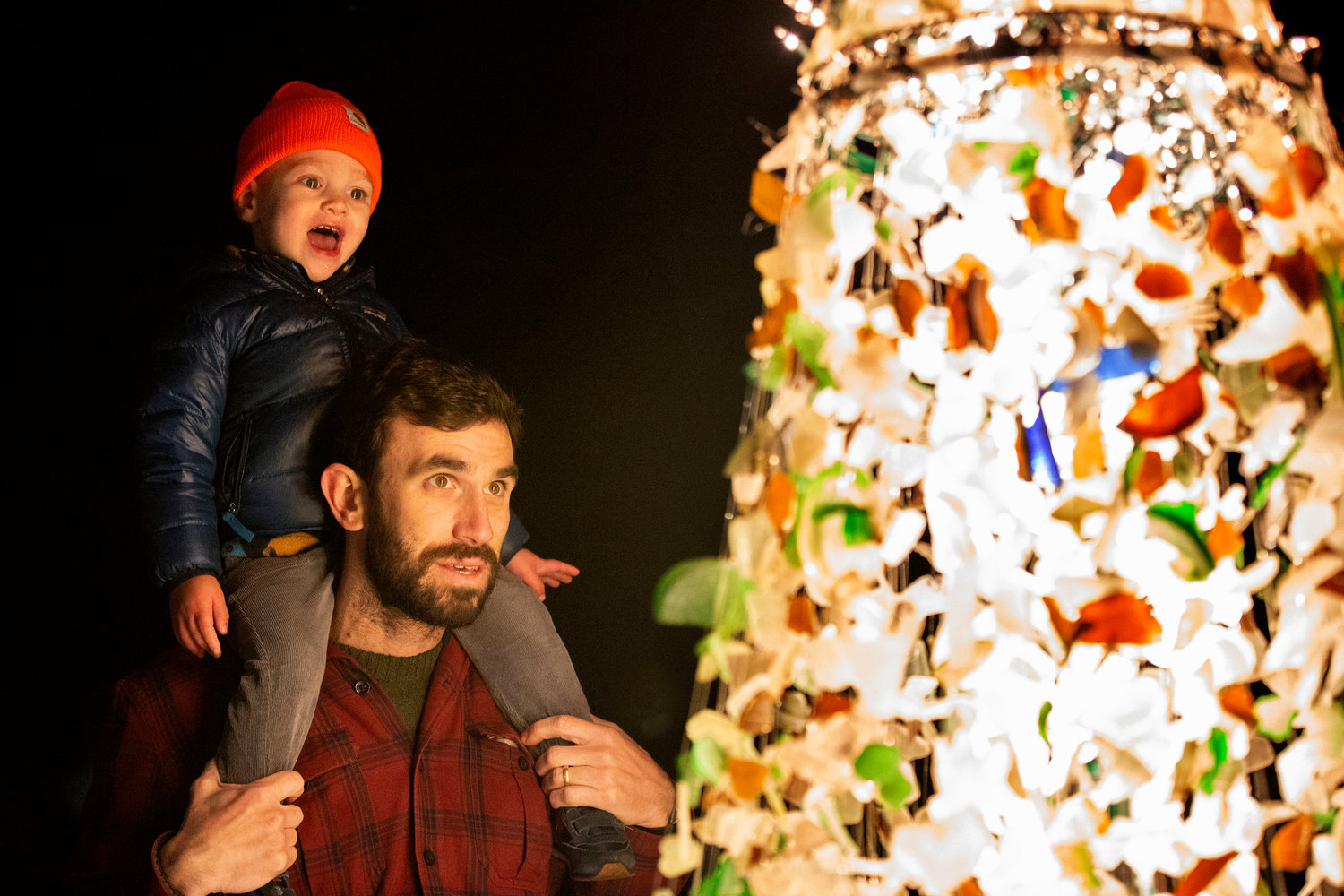 Sean Conlon and son, Remi, 2, gaze at the colorful tree made of locally found sea glass by John Viveiros and wife, Snooky.