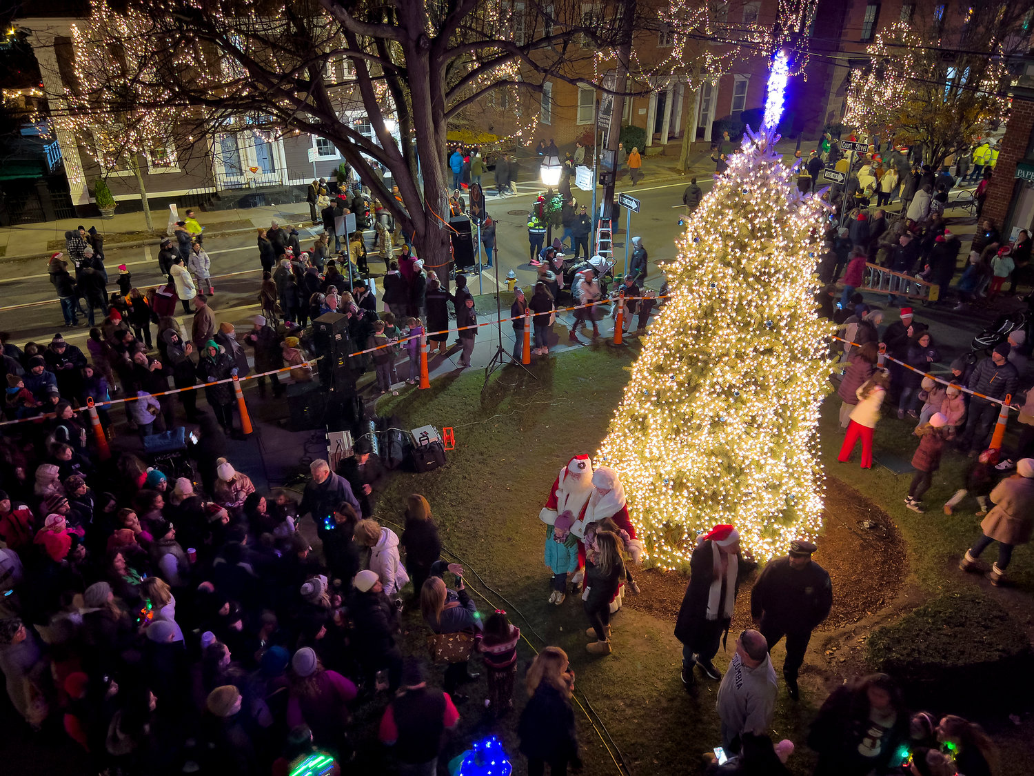 The new tree is lit for the first time, with a large crowd gathered around to witness.