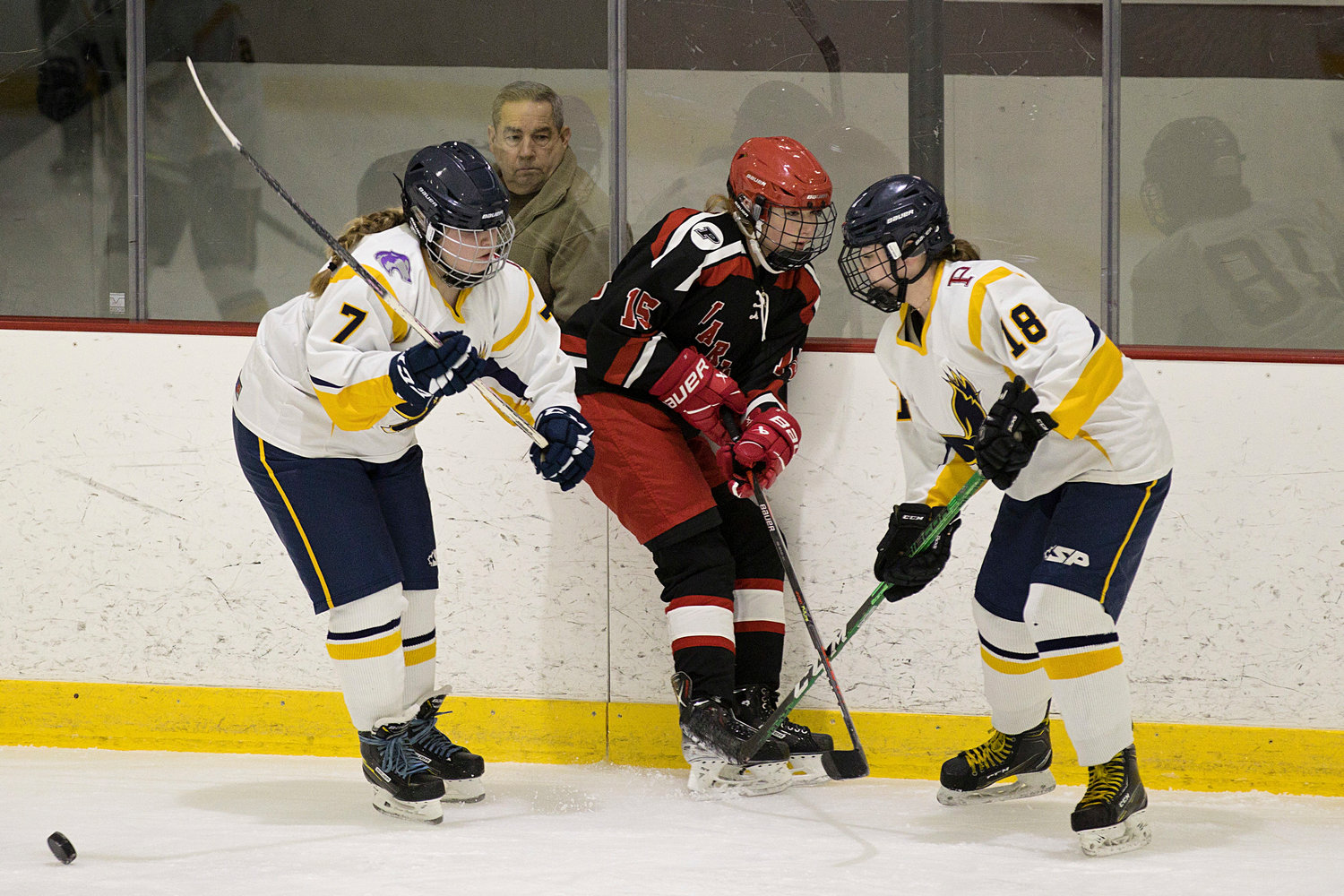 Emma Levine (left) and Hannah LeBlanc sandwich a Warwick opponent against the boards while battling for possession of the puck.