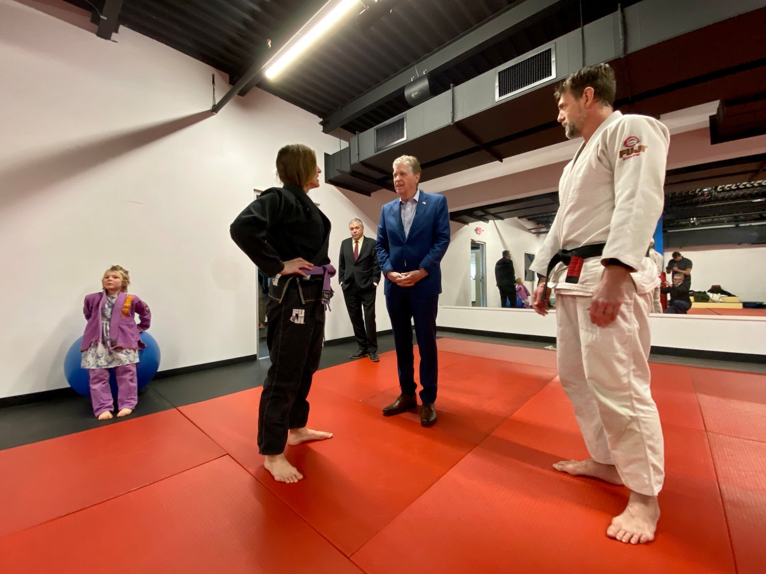 Gov. Dan McKee speaks with Jolie and Seth Hopkins; their daughter Helia is at left. The couple train children and adults in mixed martial arts and Brazilian jiu jitsu, and welcomed their first classes this past week since becoming Longplex tenants.