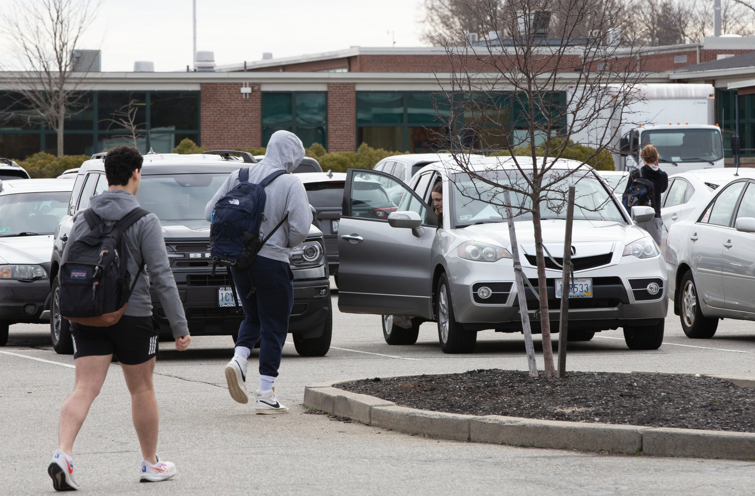 Students navigate the parking lot on foot while cars jockey for spaces.