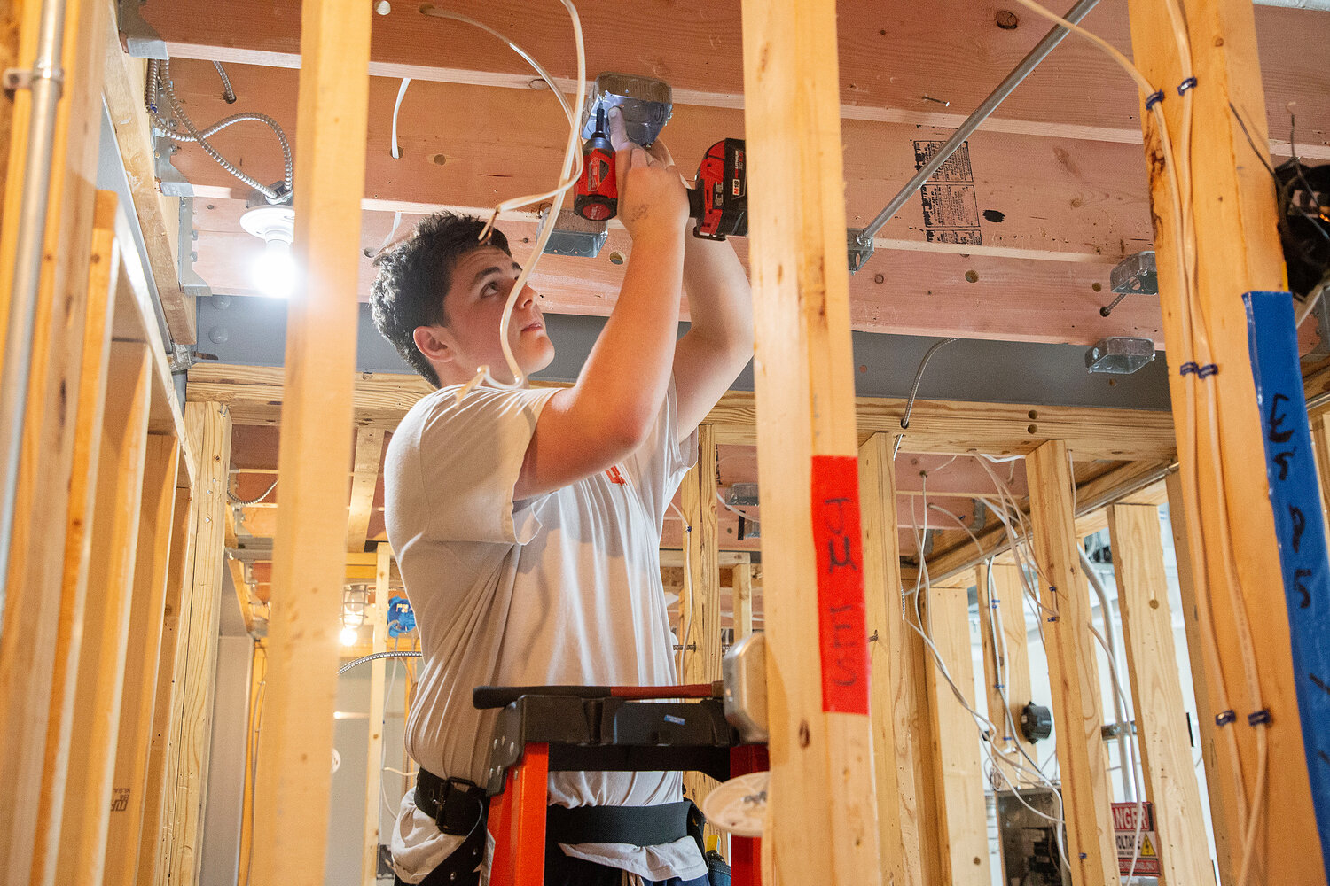 Machar Francis screws a lighting box into place inside the Electrical room at East Providence High School. Construction students framed wood stud walls within the room, and the electrical students practice both residential and commercial wiring.