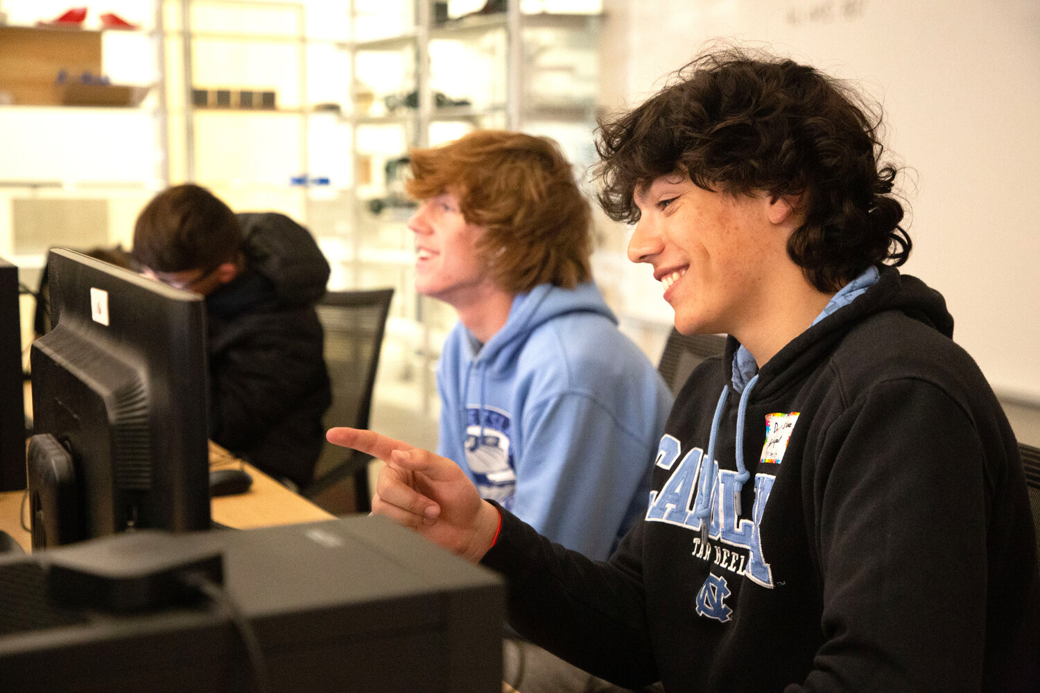 John Vaughan shares a laugh during an engineering class at East Providence High School. In the background are shelves displaying some of the products students have both designed and produced on an array of laser and 3D printers in their Engineering program.