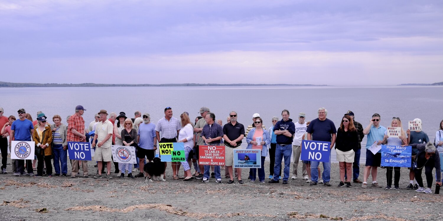 People who attended Saturday’s rally pose with signs while standing along the shoreline of Island Park Beach.
