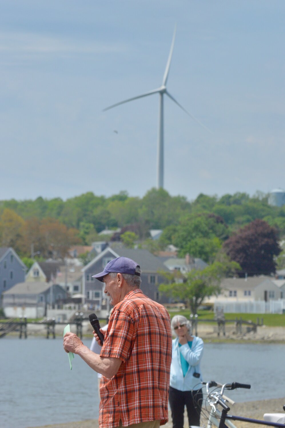 Frank Haggerty, of Jamestown, speaks to the crowd with the wind turbine at Portsmouth High School in the distance.