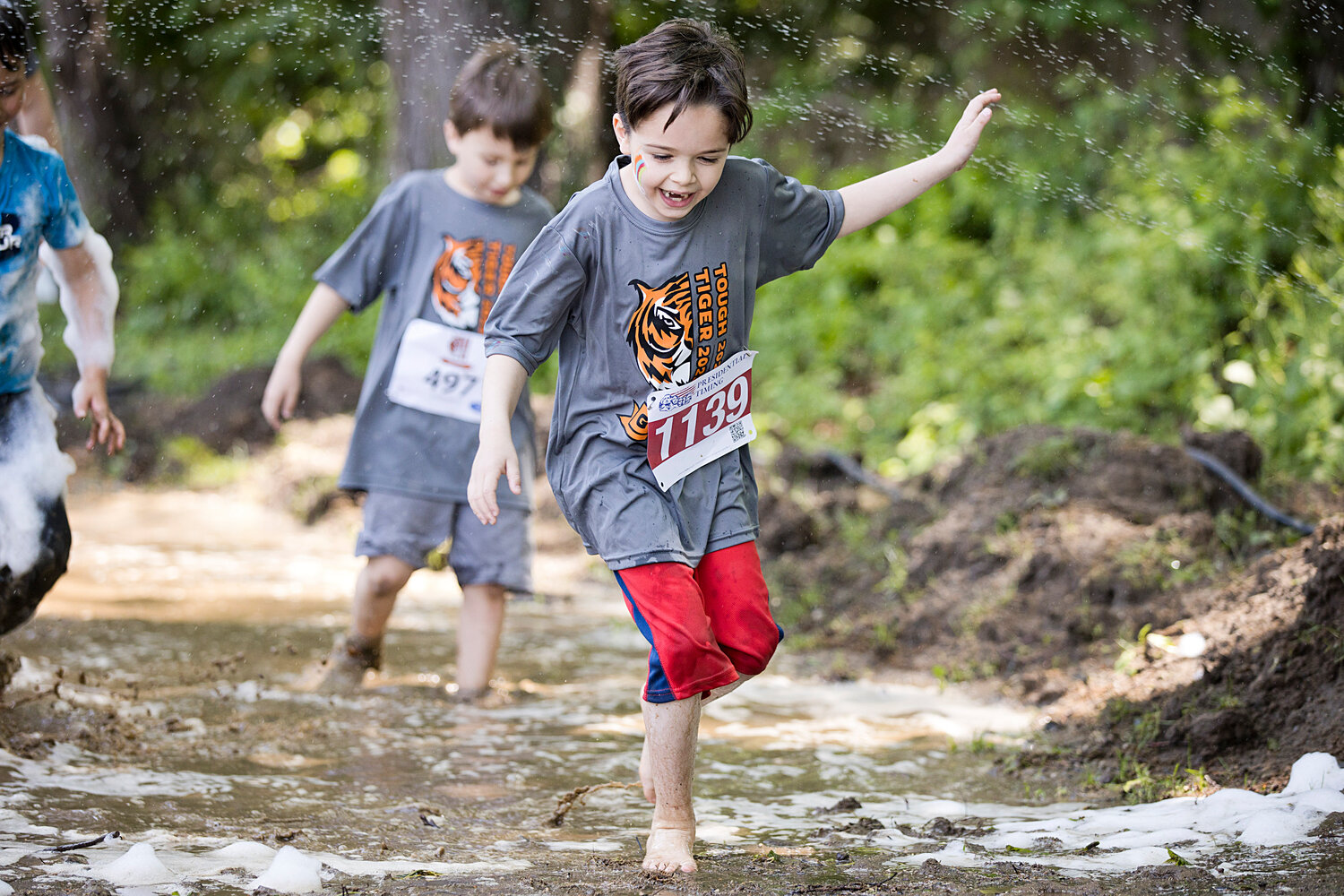A young competitor chooses to go barefoot through a muddy obstacle.