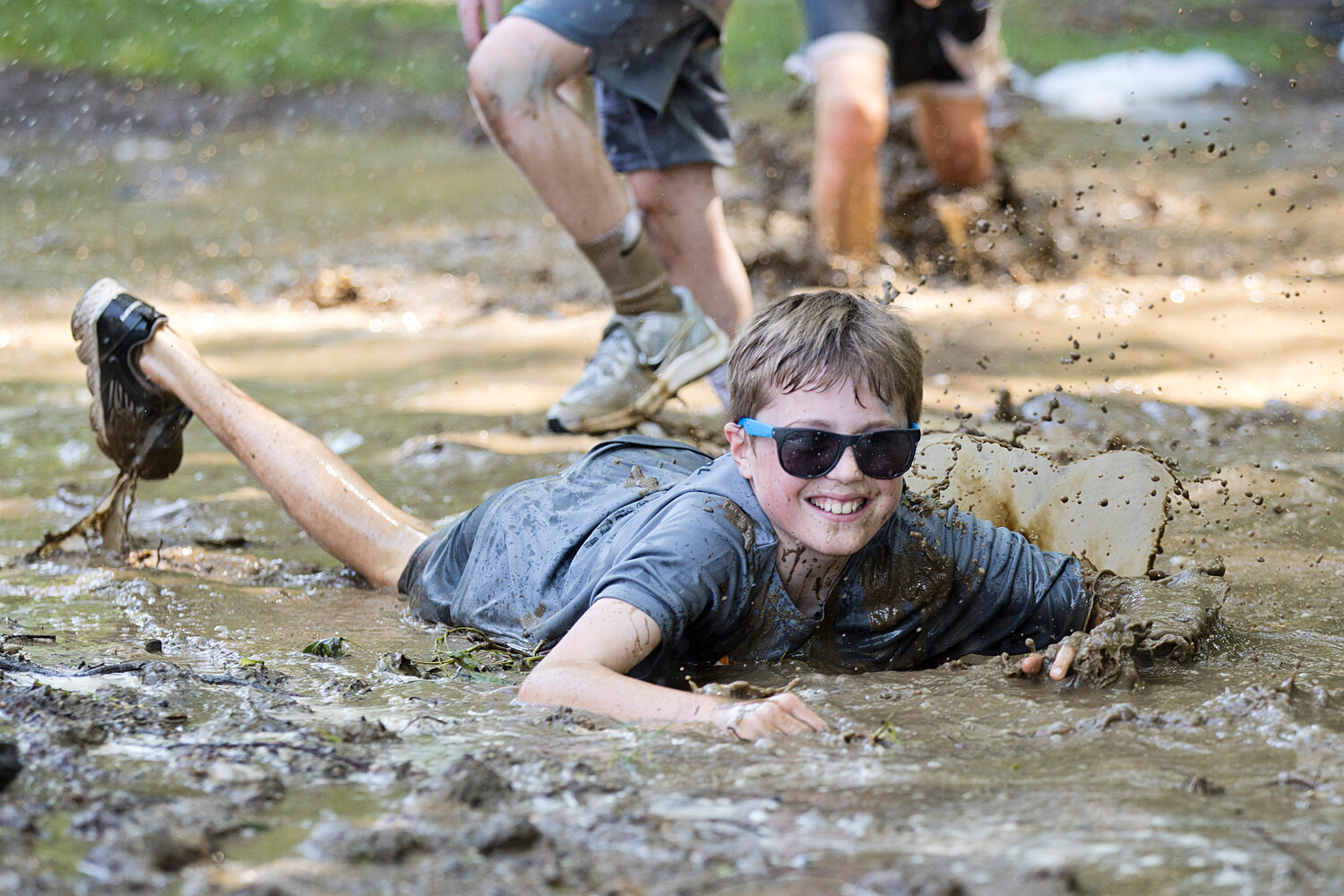 A child army-crawls through a mud obstacle in the "Tough Tiger" course.