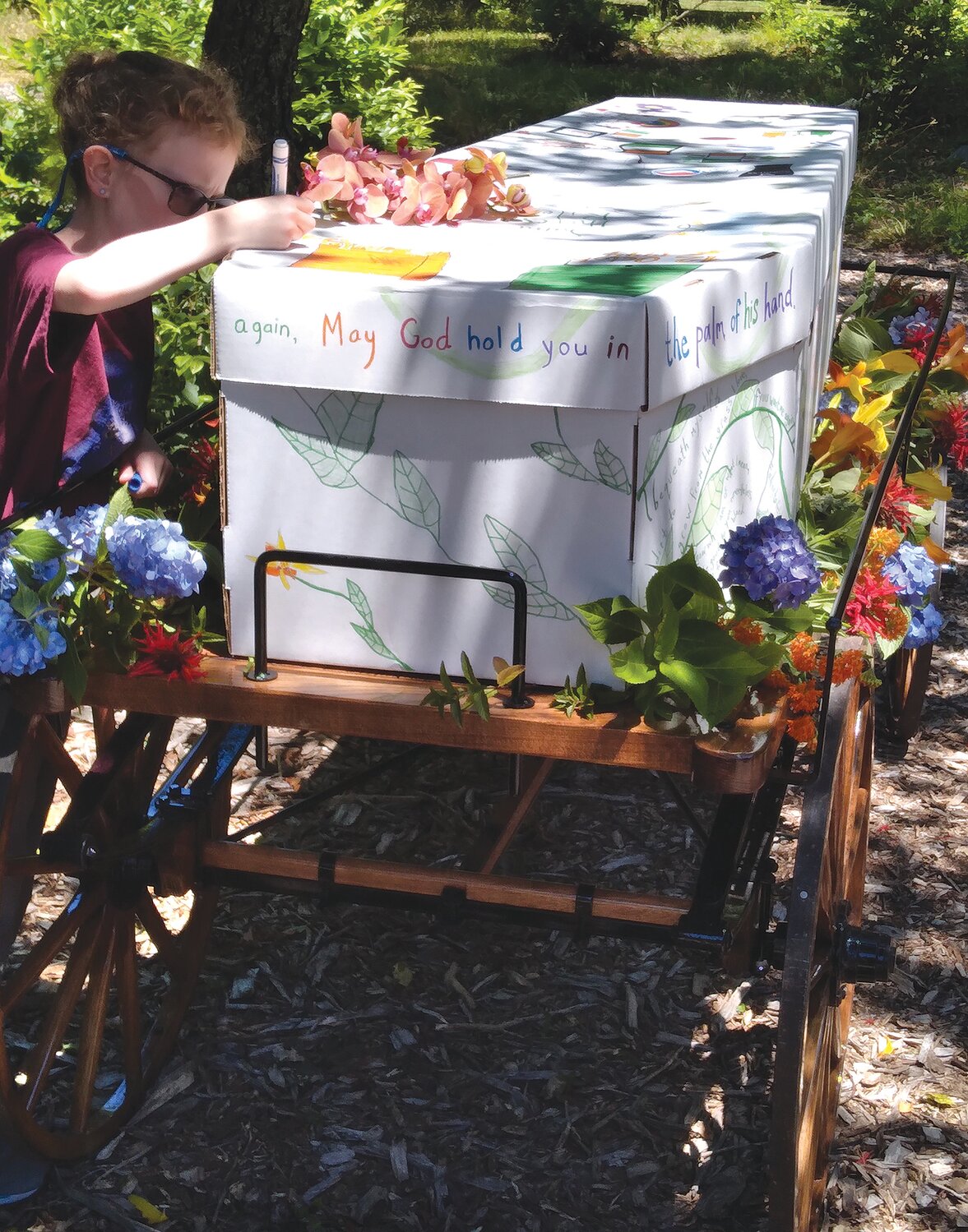 A mourner signs the outside of a coffin prior to burial at Prudence Memorial Park. “Natural” burial grounds like this use biodegradable coffins, no embalming, and allow the burial site to revegetate naturally. Memorial plantings of native species are welcomed.