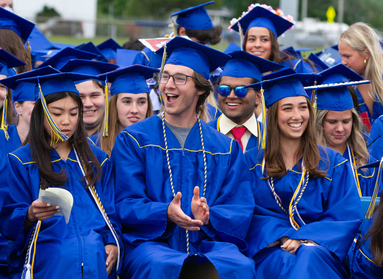 Charlie Whittaker (center) cheers during Sunday’s graduation ceremony at Barrington High School, while Katie Byon (left) and Sonya Pareek (right) sit nearby.
