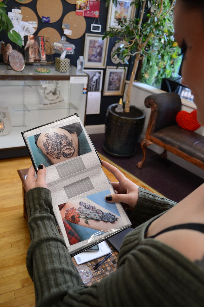 Chrystal Santos flips through a book showing some examples of past tattoos she has designed and performed for clients. A skilled artist since she was a child, Santos has been perfecting her craft since beginning with a senior project while in high school in Tiverton.