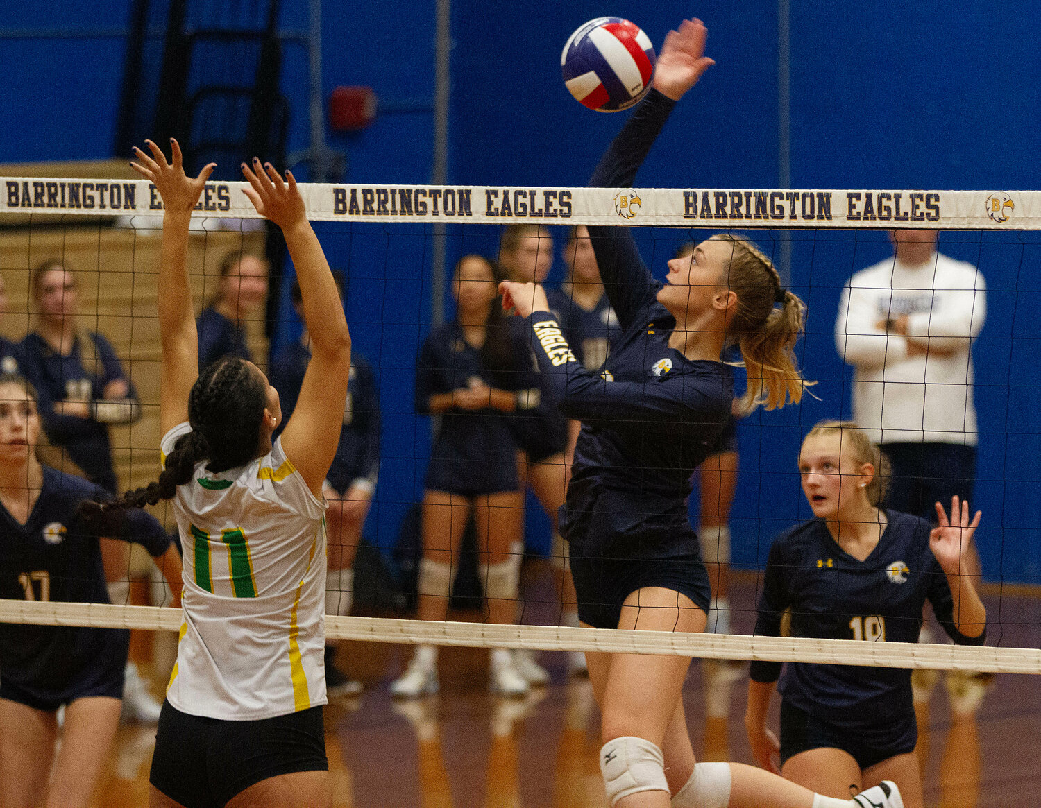 Ruby Ciummo elevates to spike the ball over the net with Ava Hentz (left) and Sophia Denham looking on.
