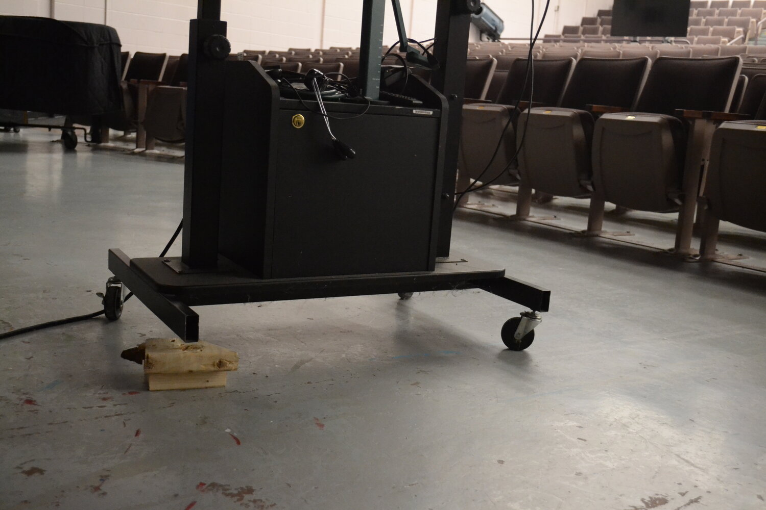 A projector cart is stabilized on a wood block in the school's auditorium.